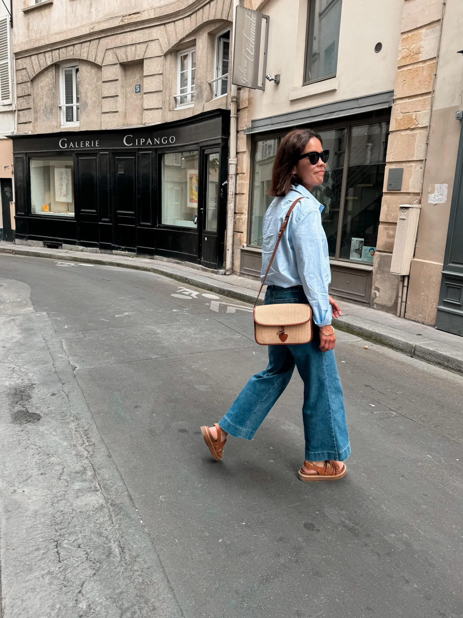 Woman in blue button down with jeans, raffia bag.