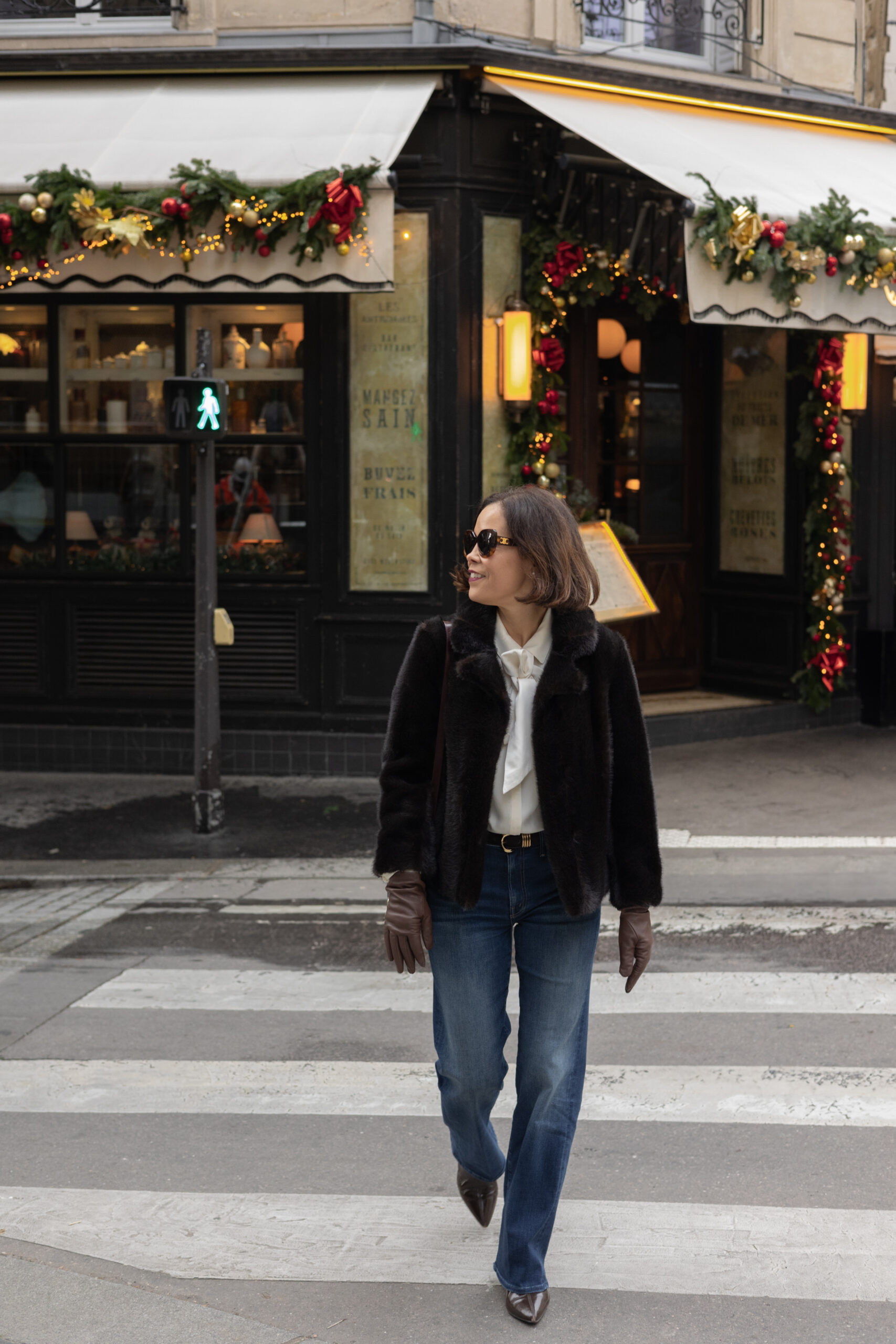 Woman wearing straight leg denim with brown fur coat walking arcross the street.