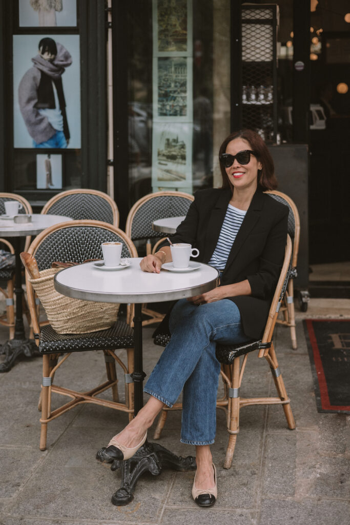 Woman sitting at a cafe with a black blazer and stripe shirt.