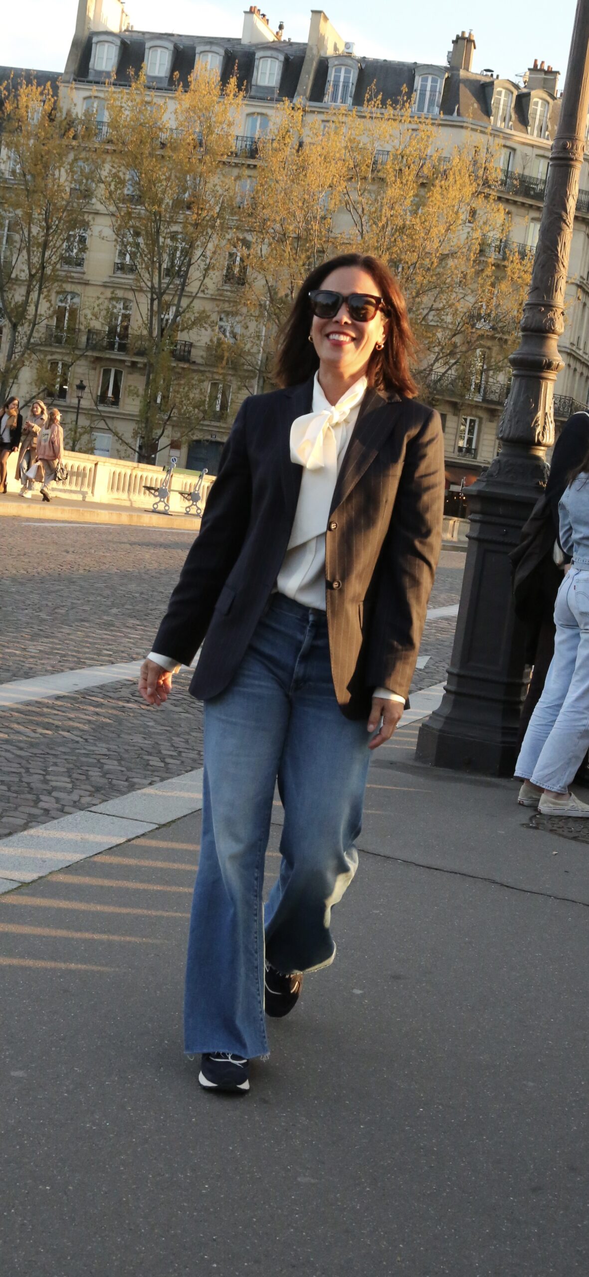 Woman wearing wide leg denim with sneakers and a blazer.