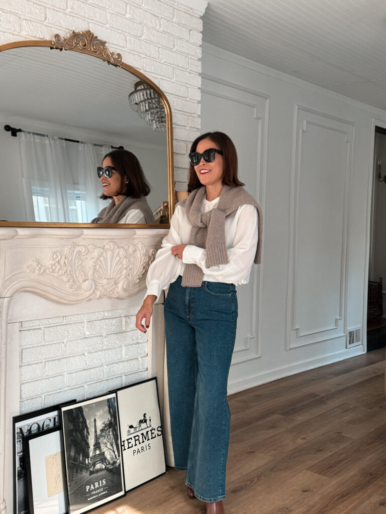 Woman wearing denim and silk top against fireplace.