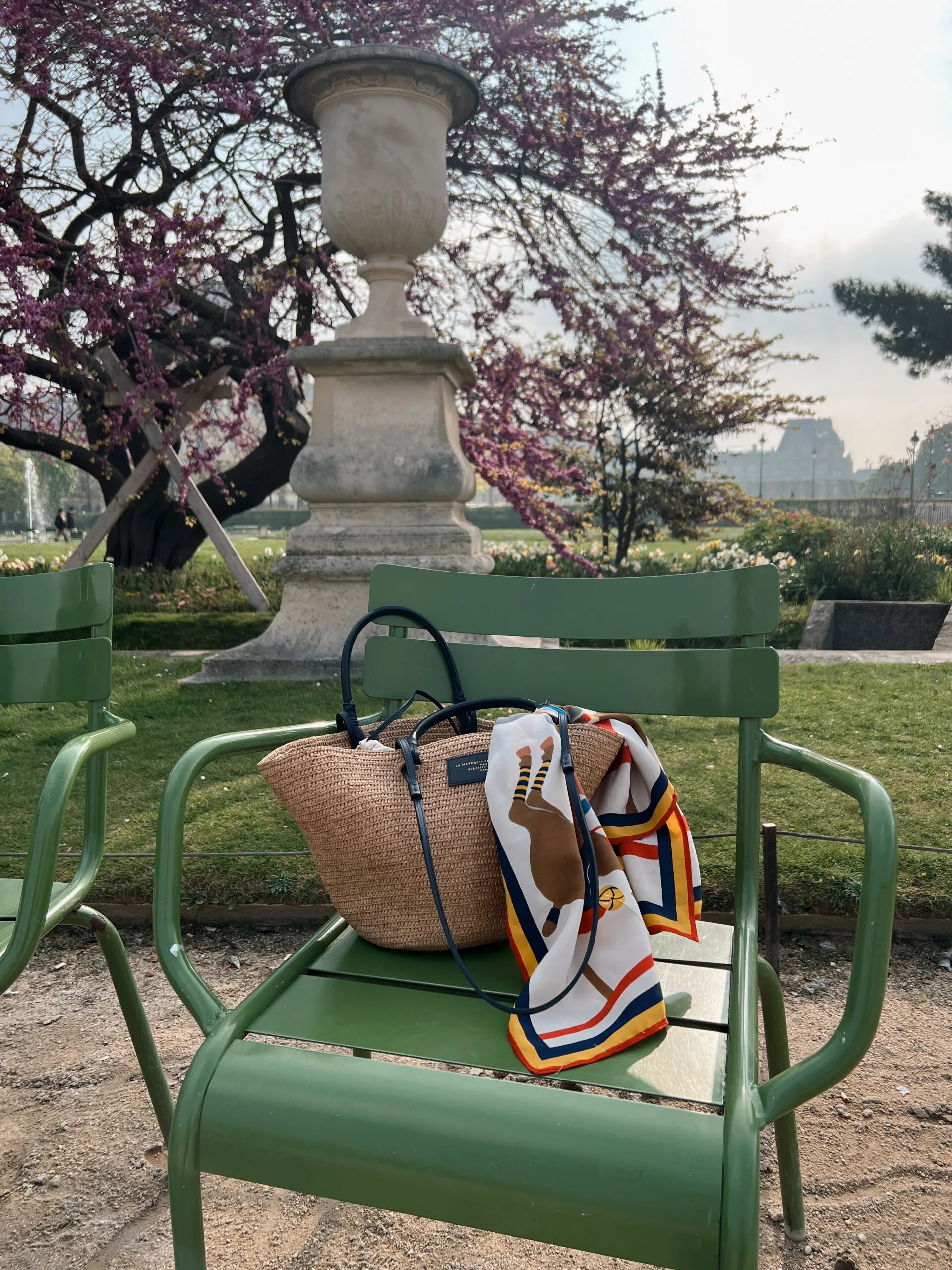 Summer bag with scarf on a green chair in the park which shows french girl summer essentials to wear.