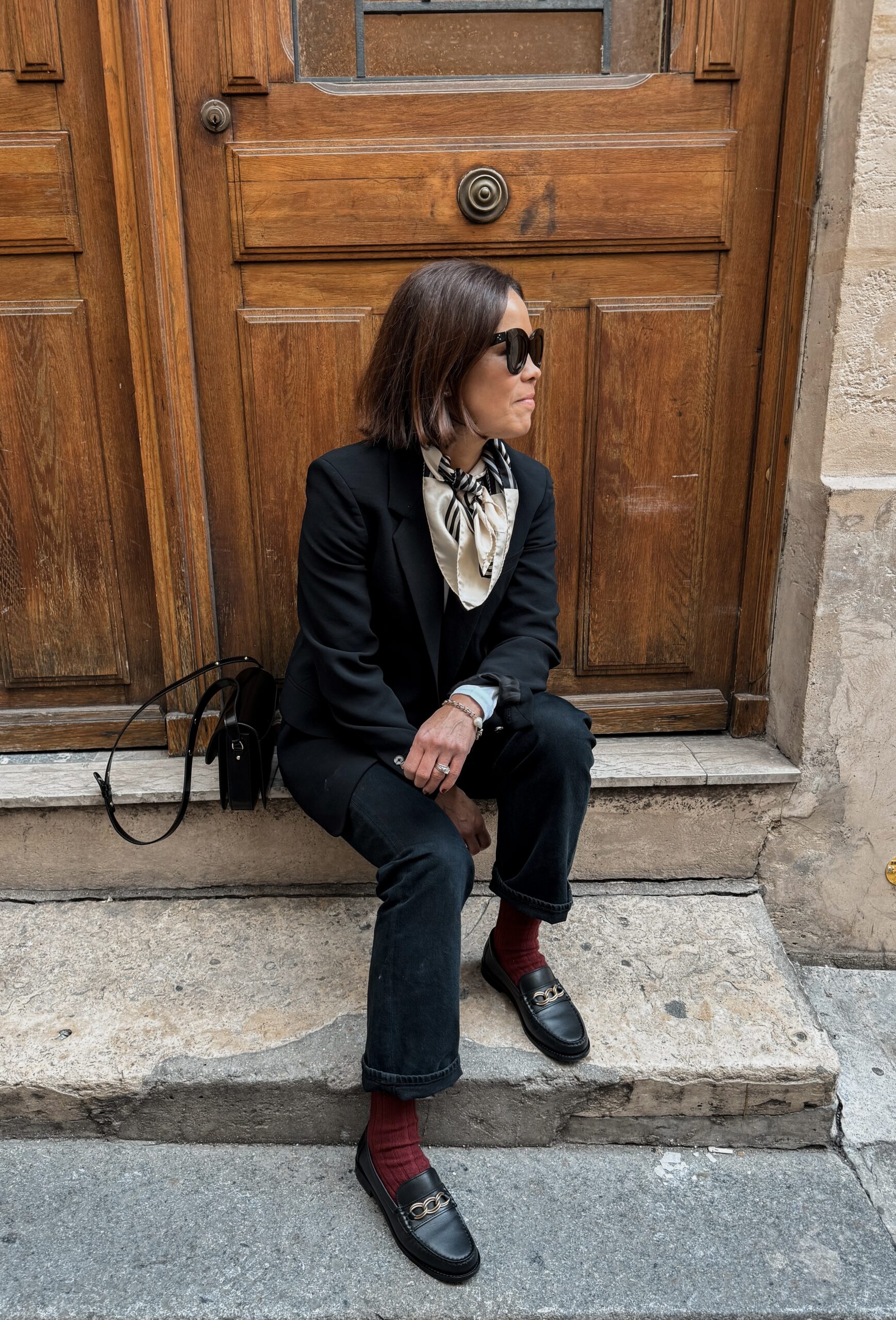 Woman wearing black blazer with scarf and red socks sitting in Paris.