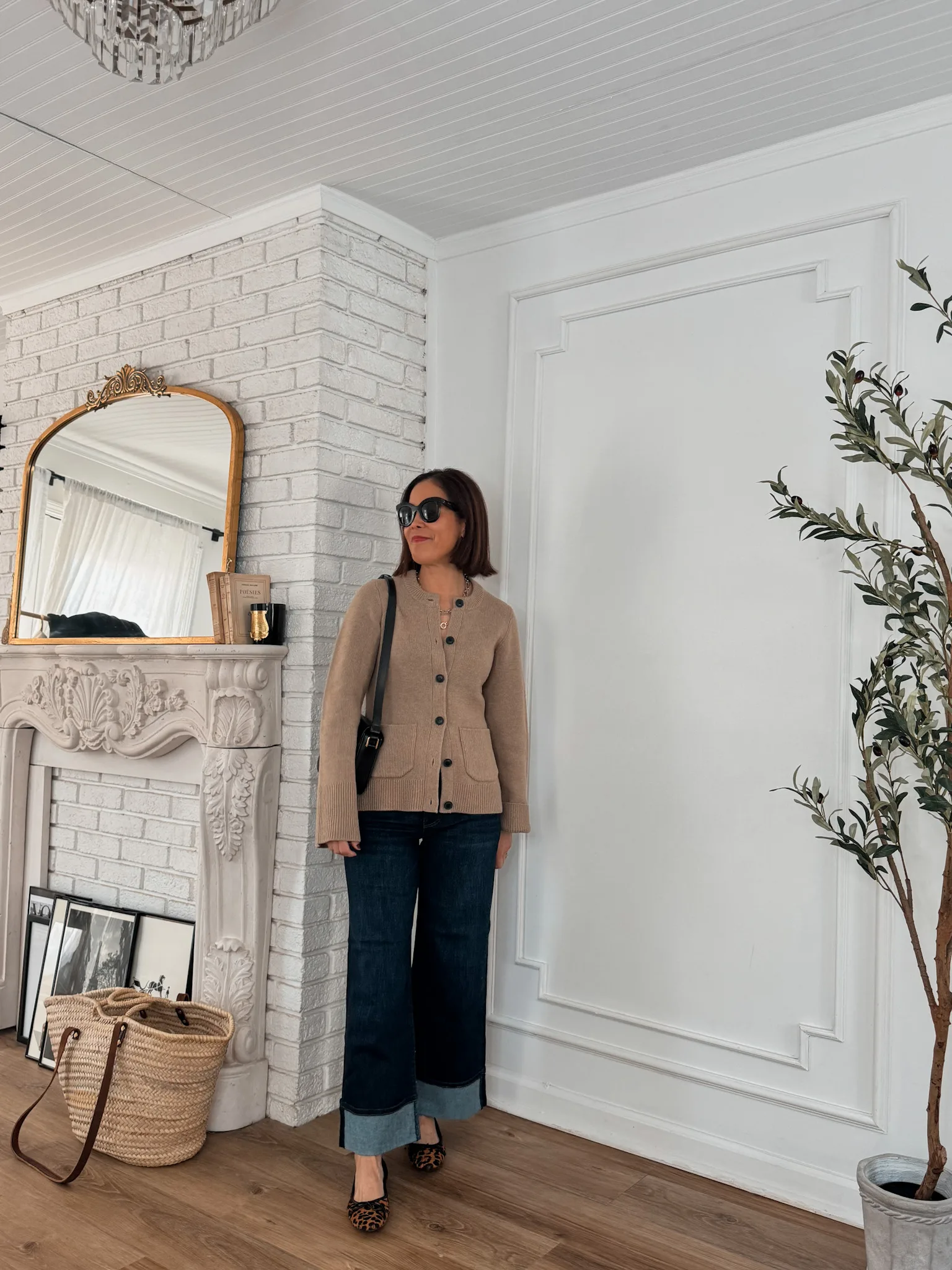 Lady in a cardigan and dark denim standing in a corner of a room.