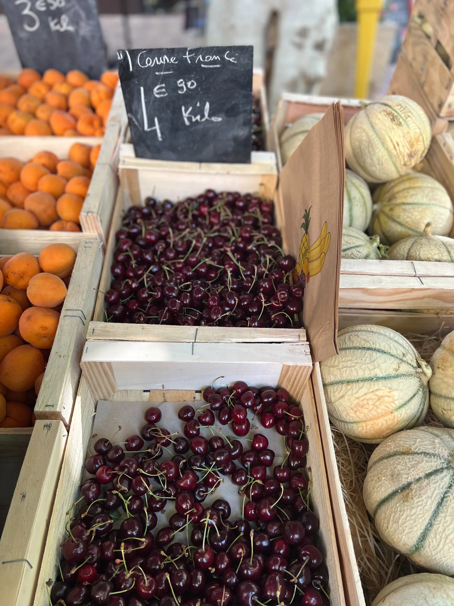 Basket of cherries along with cantalope and oranges at a farmers market.