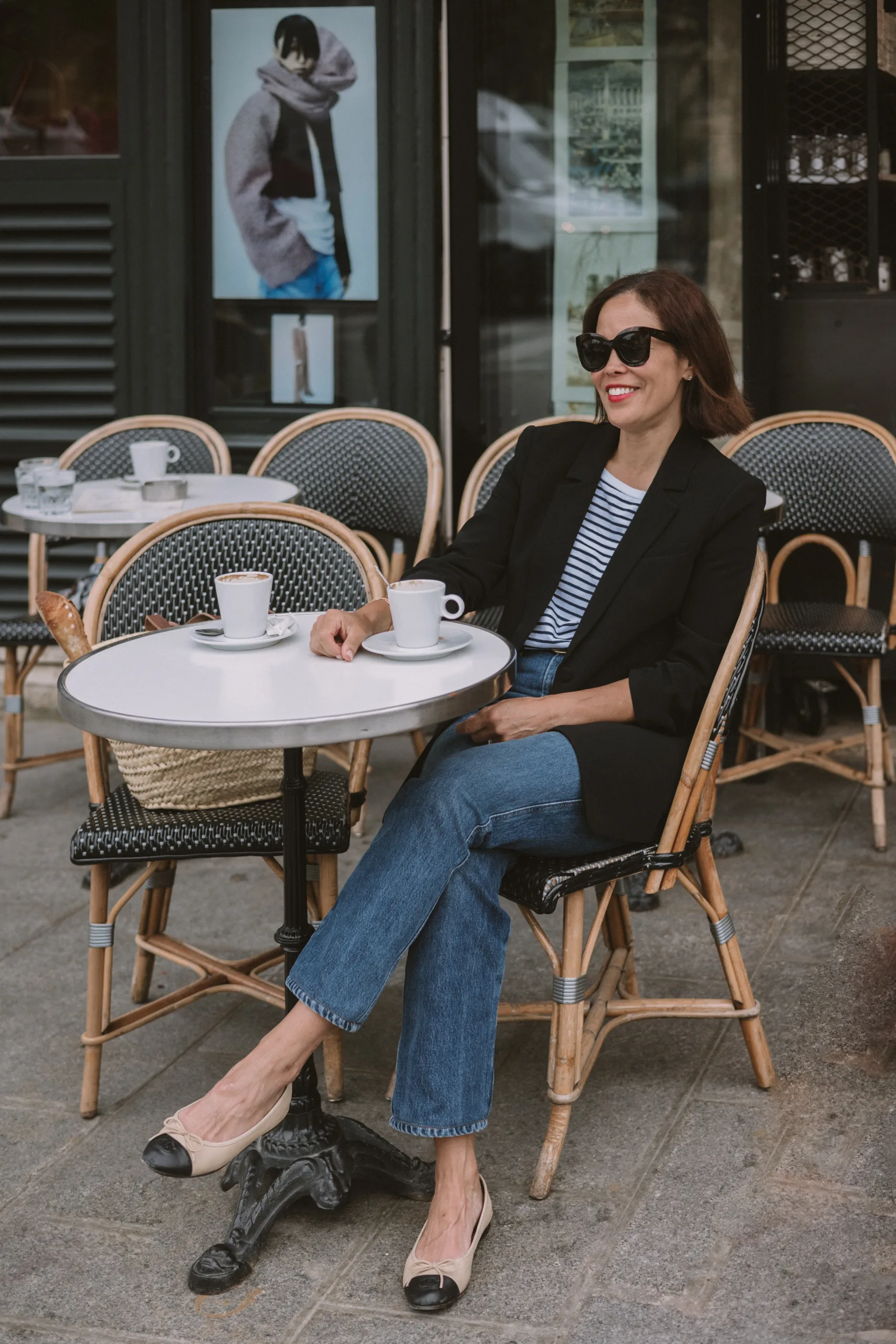 Woman sitting at a cafe with black blazer, ballet flats and denim in paris.