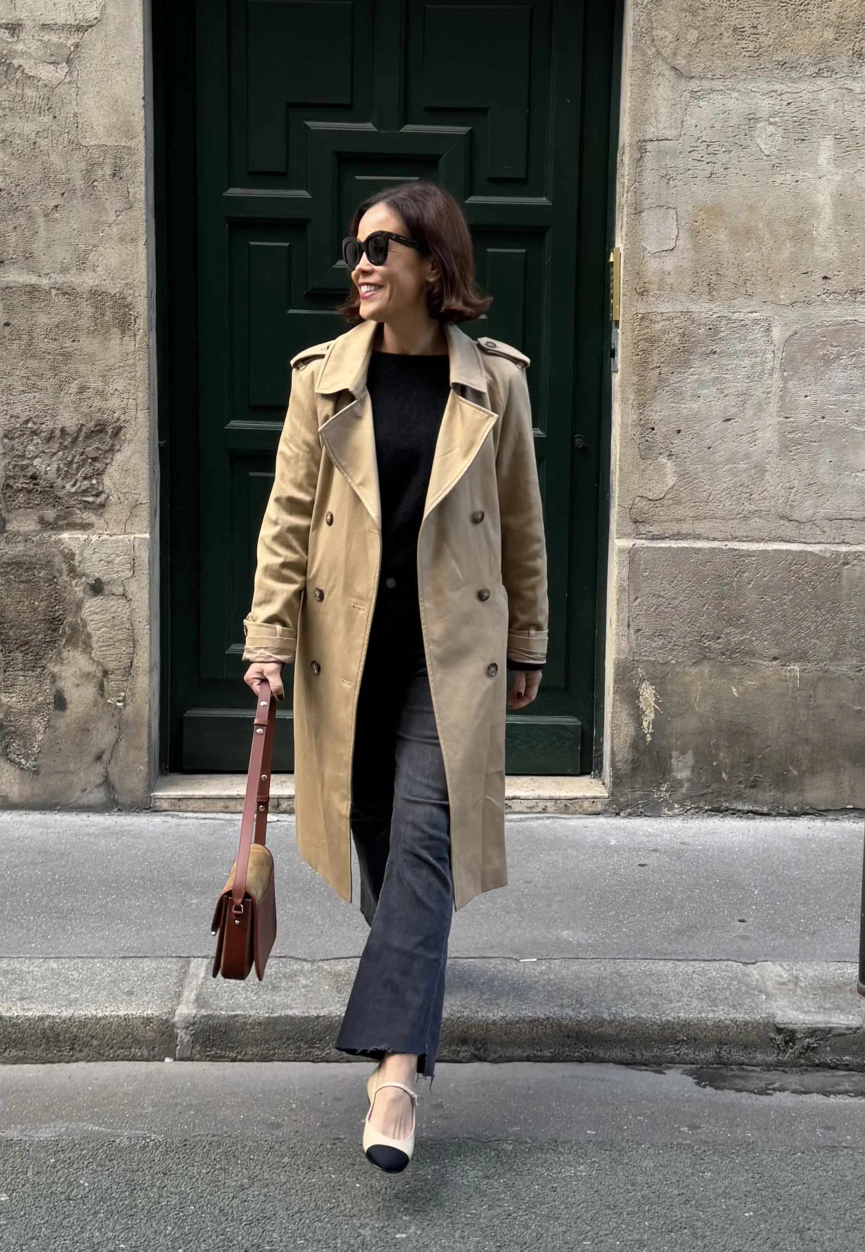 Woman wearing trench coat with ballet flats walking off a curb.