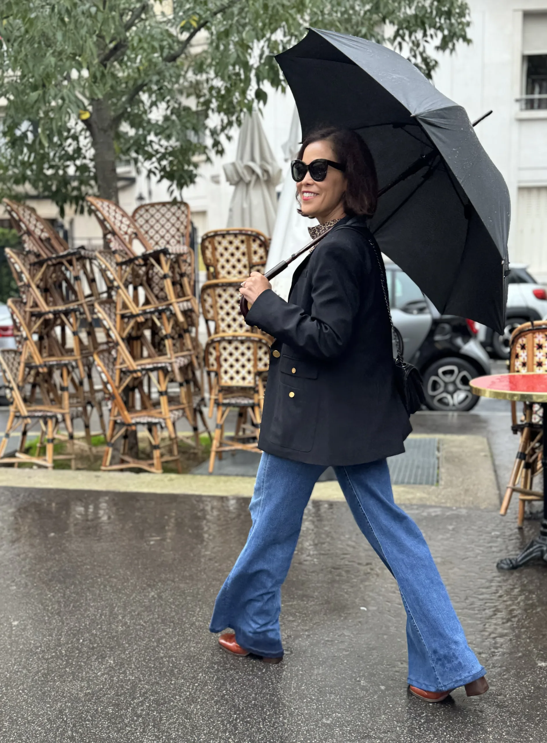 Woman carrying umbrella walking in front of stacked chairs in paris.
