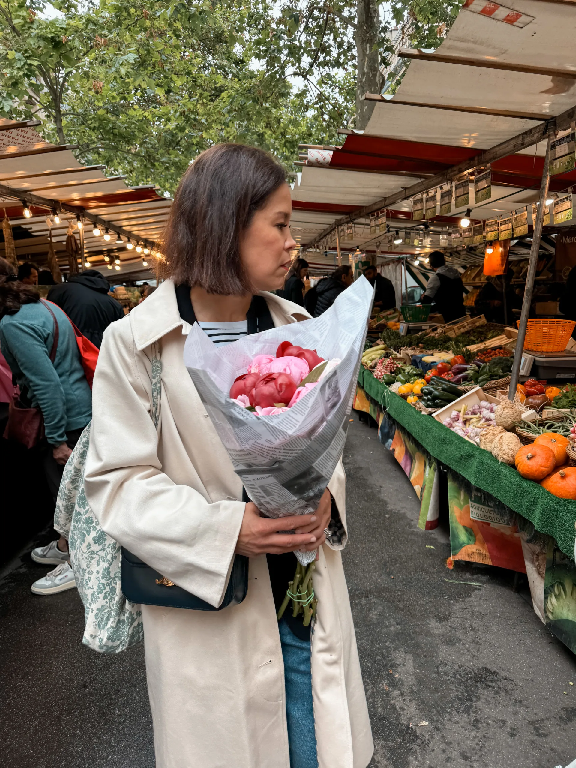 Woman wearing an ecru trench coat carrying flowers at a market in paris.