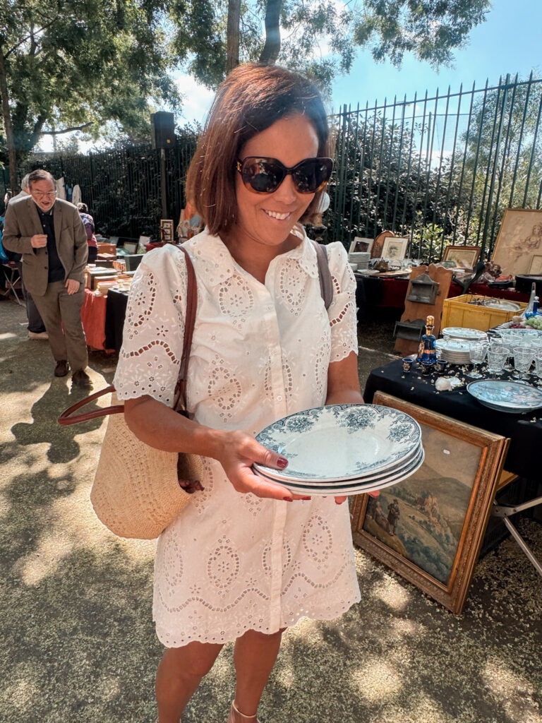 Woman at a flea market in Paris wearing a white eylet dress holding plates. 