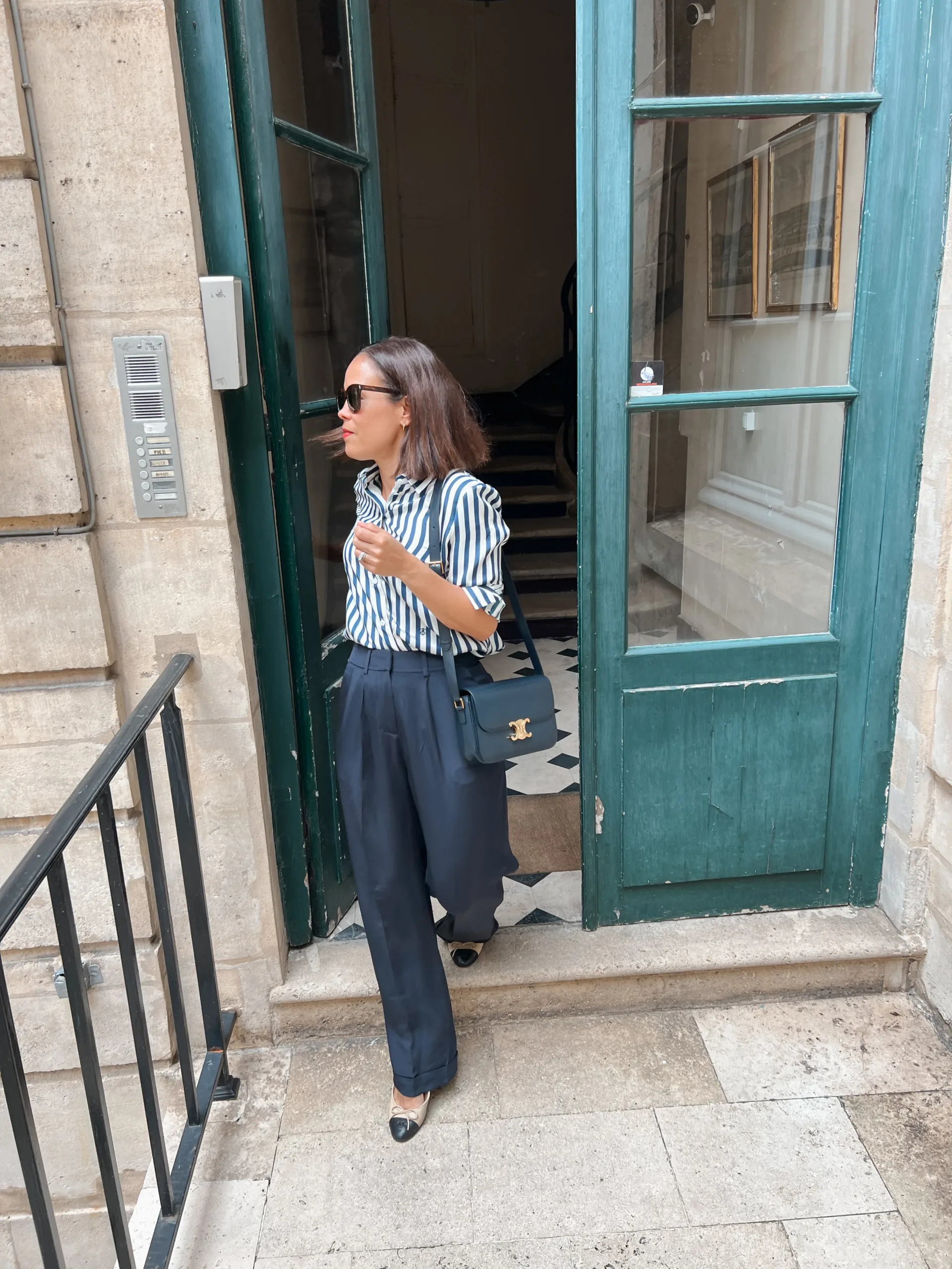 Woman wearing navy and stripe silk top with trousers coming out of building in Paris.