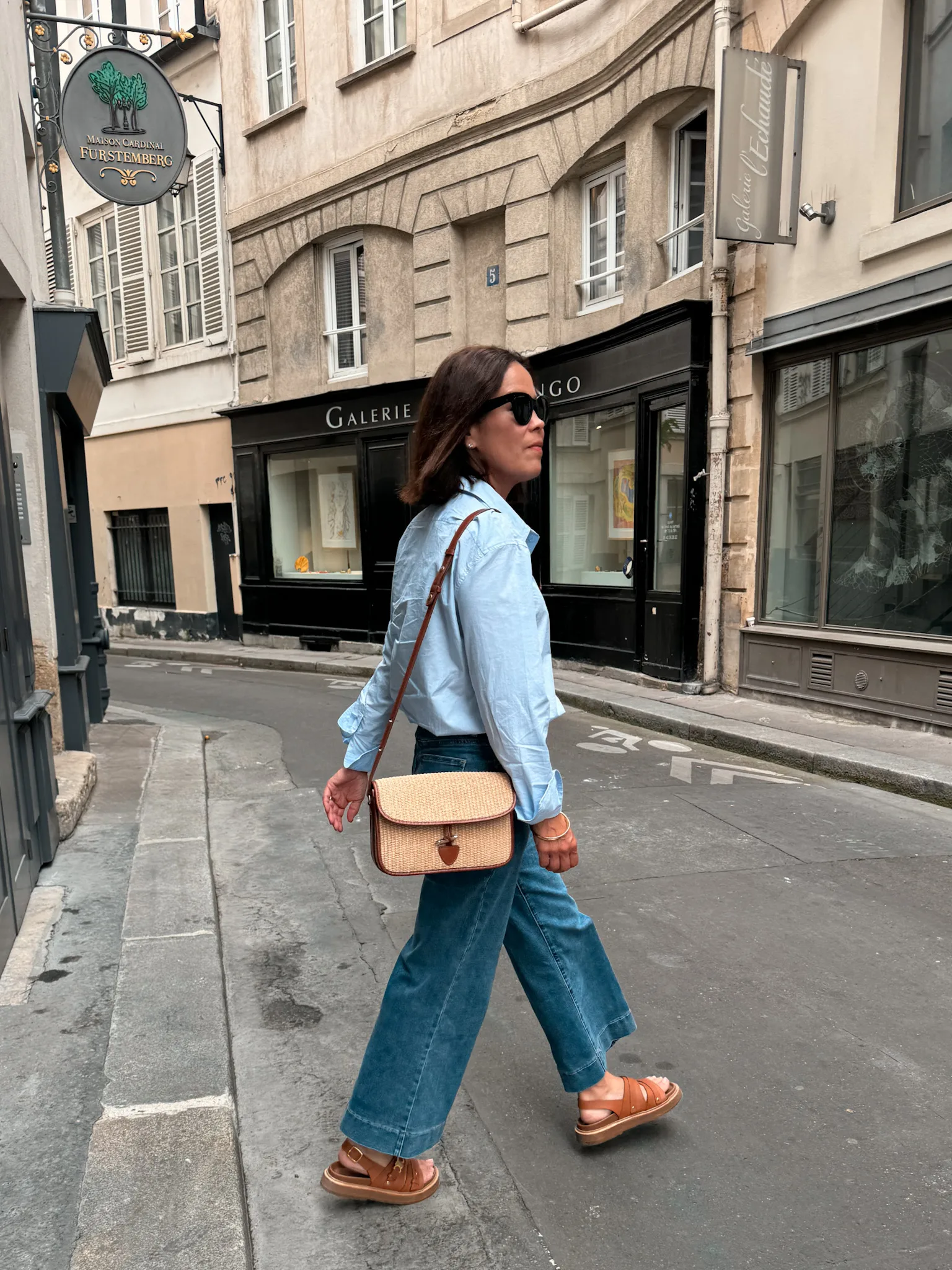 Woman walking wearing blue oxford button down with crop denim and sandals. 