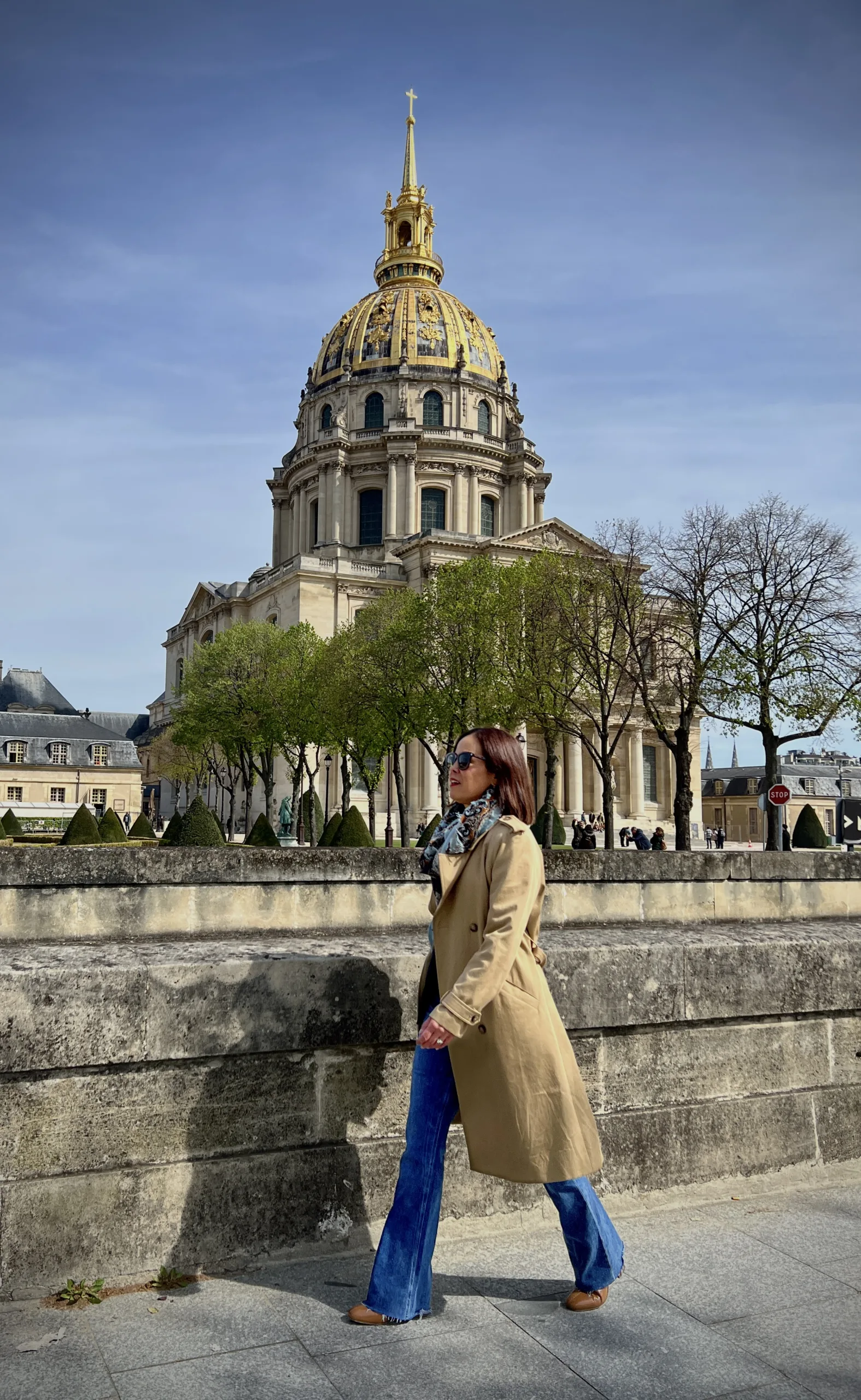 Woman walking wearing a  trench coat in Paris with a scarf and boots.