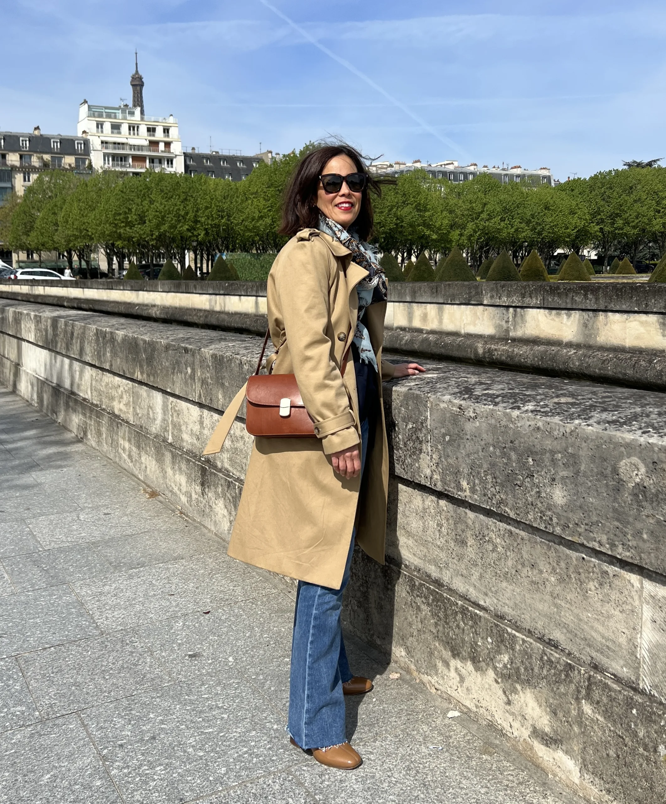 Woman wearing trench coat with boots and handbag.