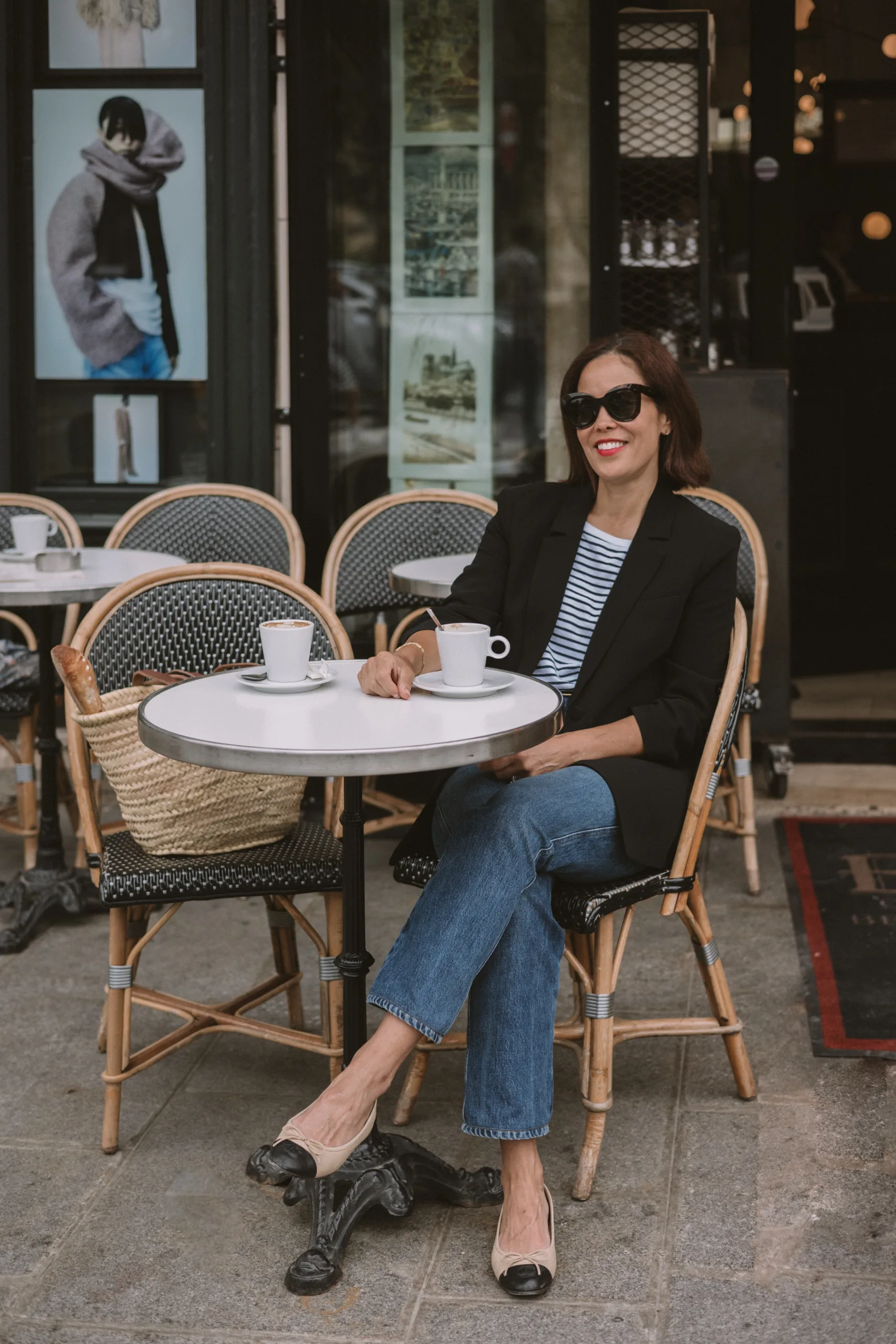 Woman wearing stripe top with black blazer and flats sitting at a cafe.