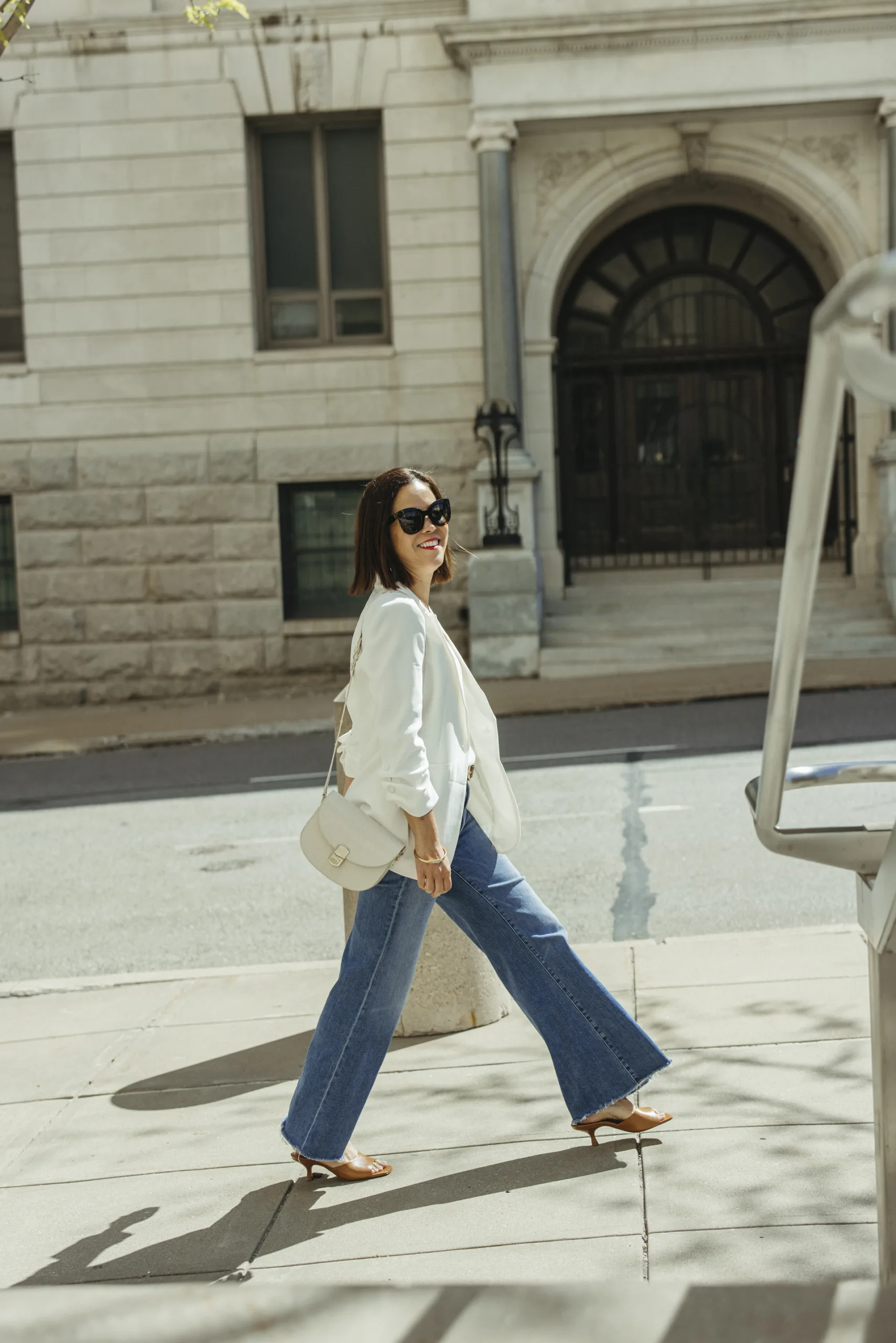 Woman wearing white blazer with denim and white bag.