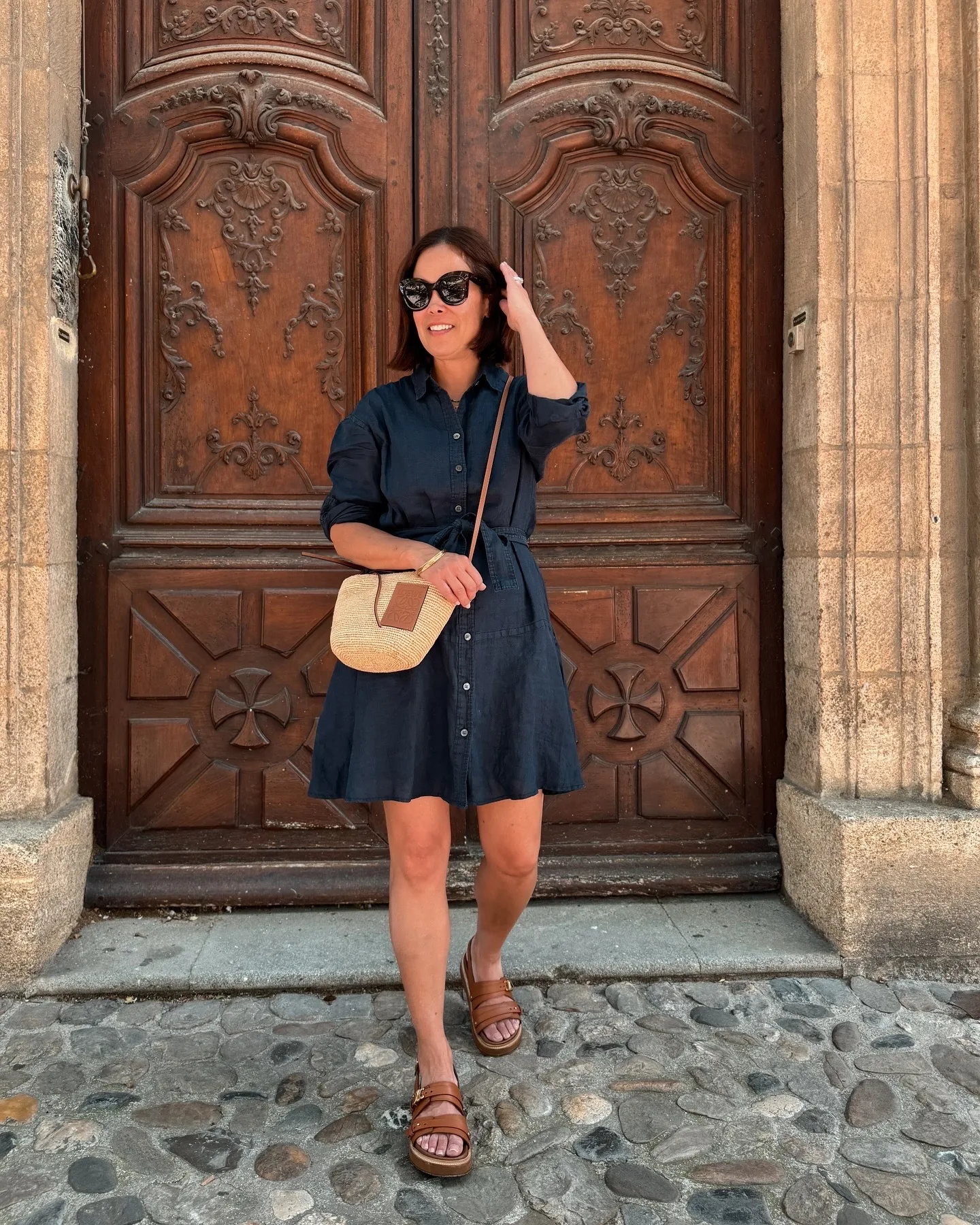 women in a navy dress with sandals in front of a big brown door in Provence.