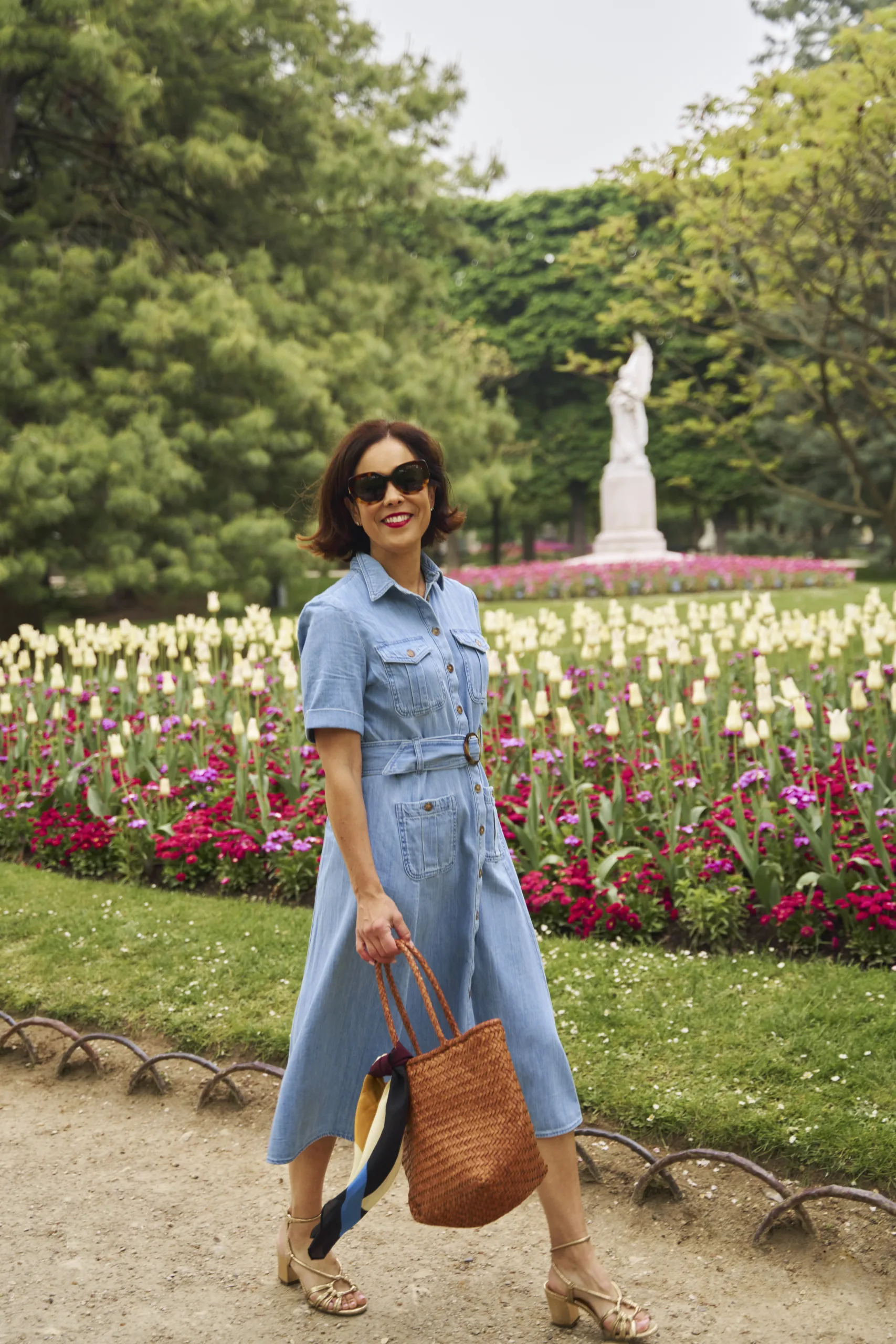 Woman walking in garden with flowers and denim dress.