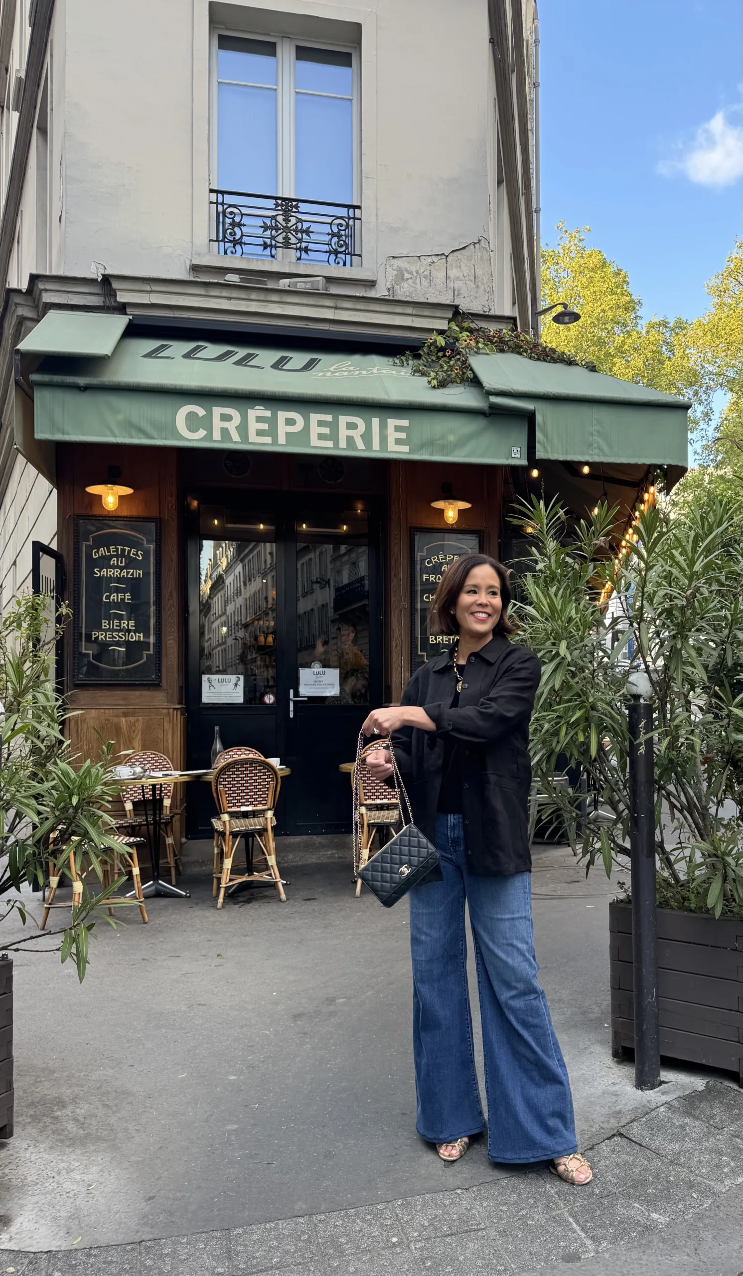 Woman wearing black jacket with denim and gold sandals.