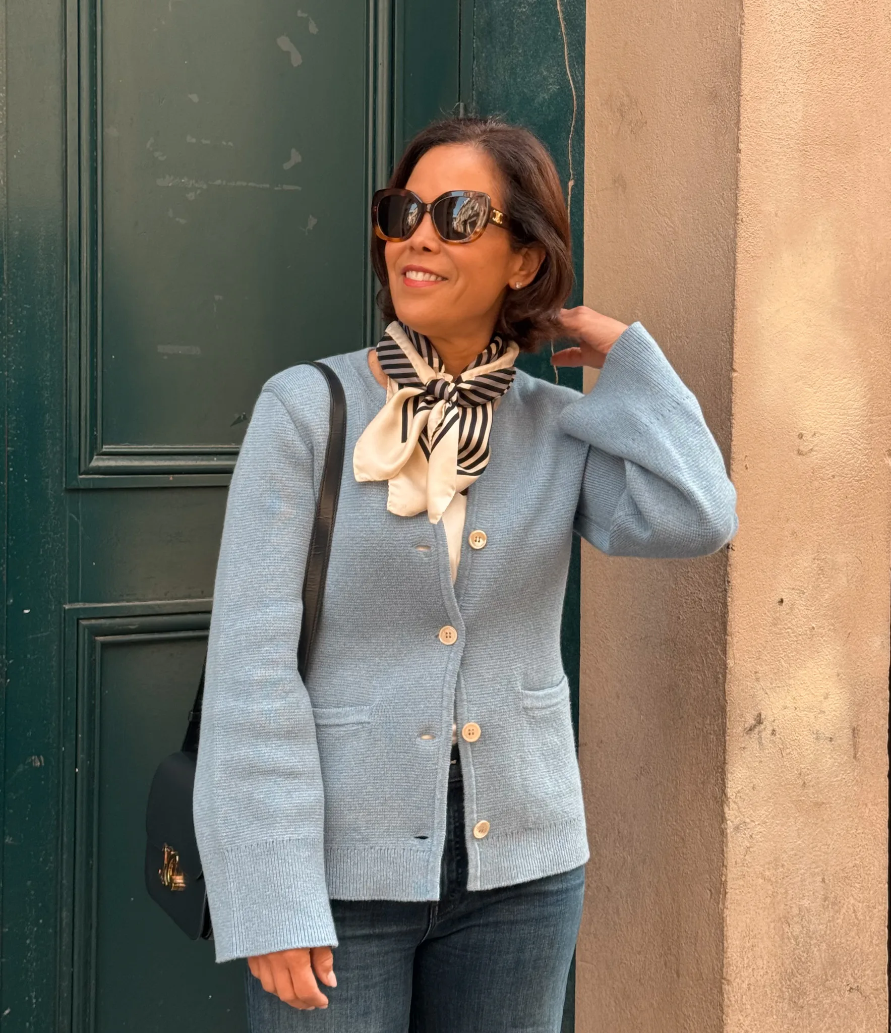Woman wearing blue cardigan with scarf and denim in Paris in April.