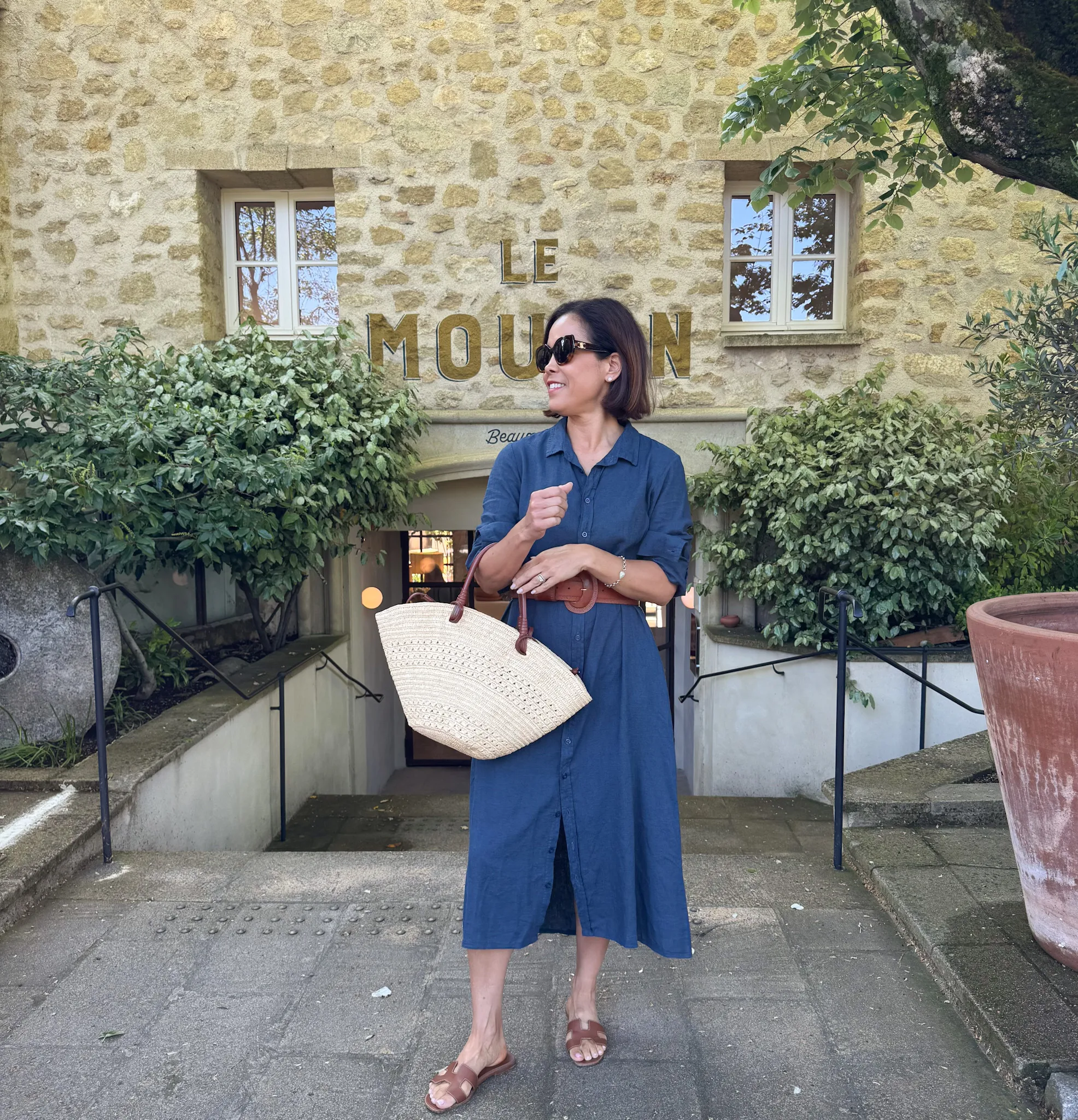 Woman in navy dress with brown sandals and carrying a woven tote.