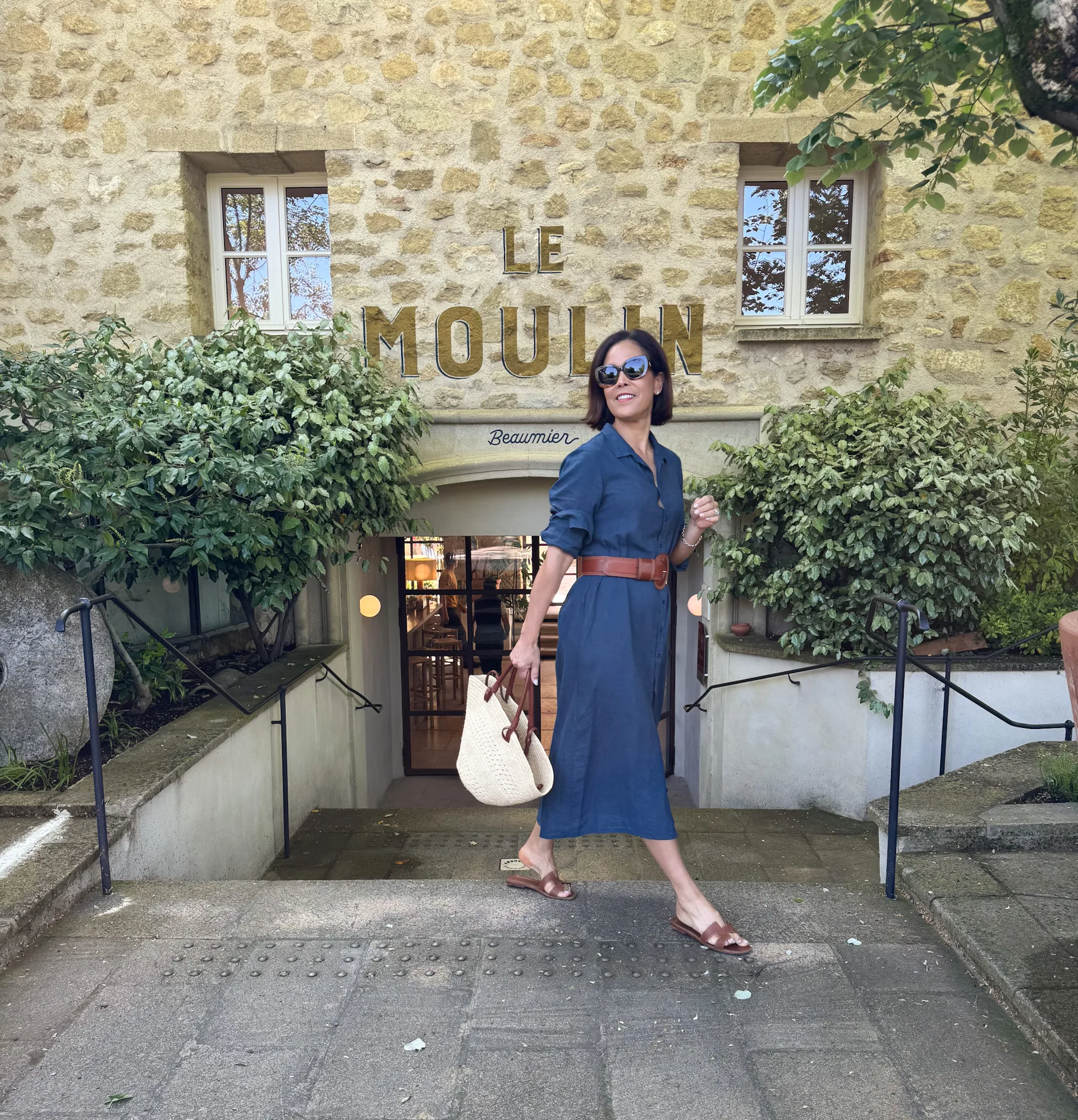 Woman wearing navy dress with brown sandals and a belt.