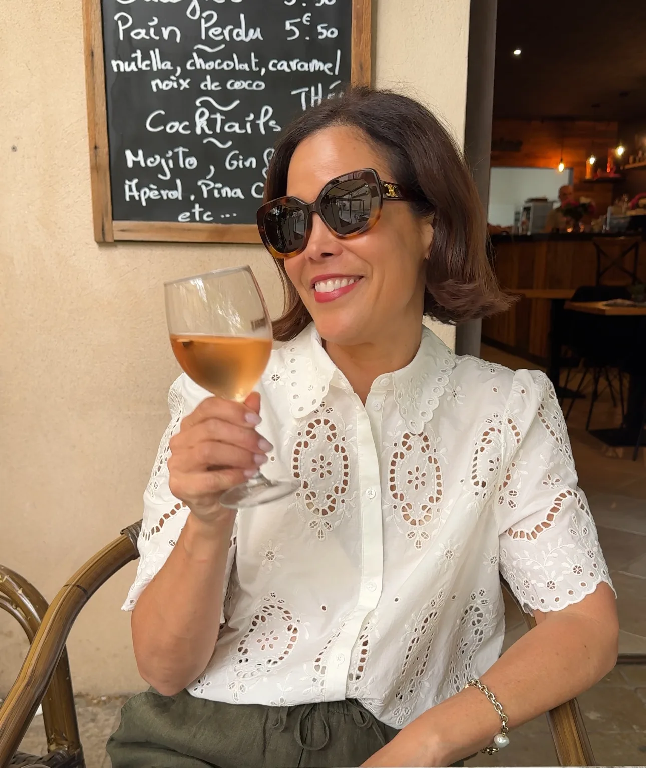 Woman wearing eyelet top and holding a glass of wine.
