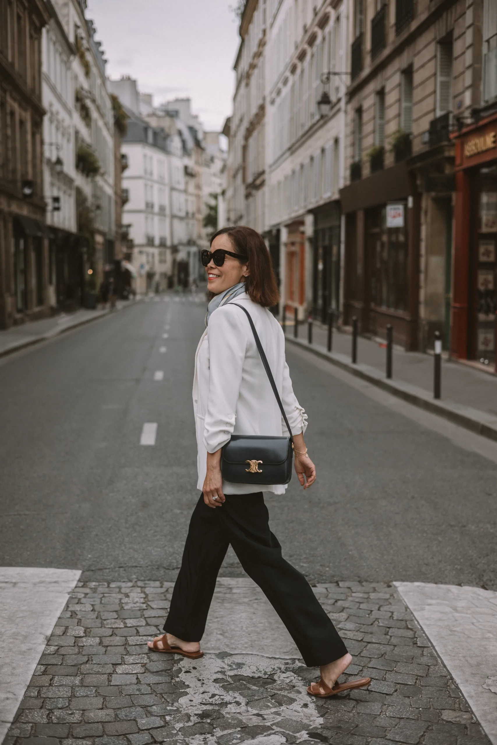 Woman walking in Paris with navy pants and white blazer.