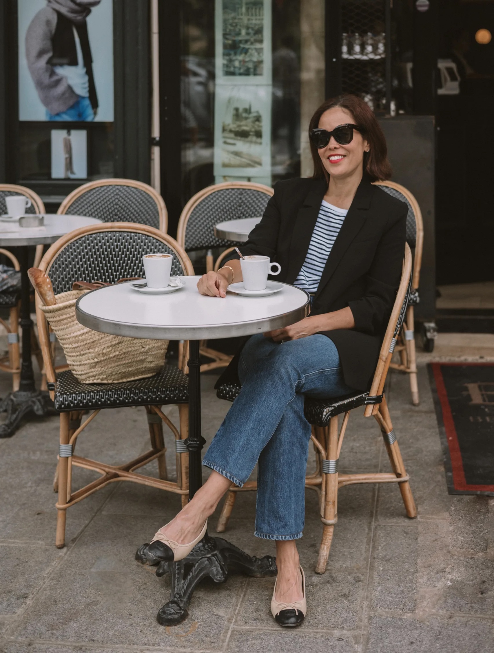 Woman wearing black blazer with denim sitting at a cafe in paris.