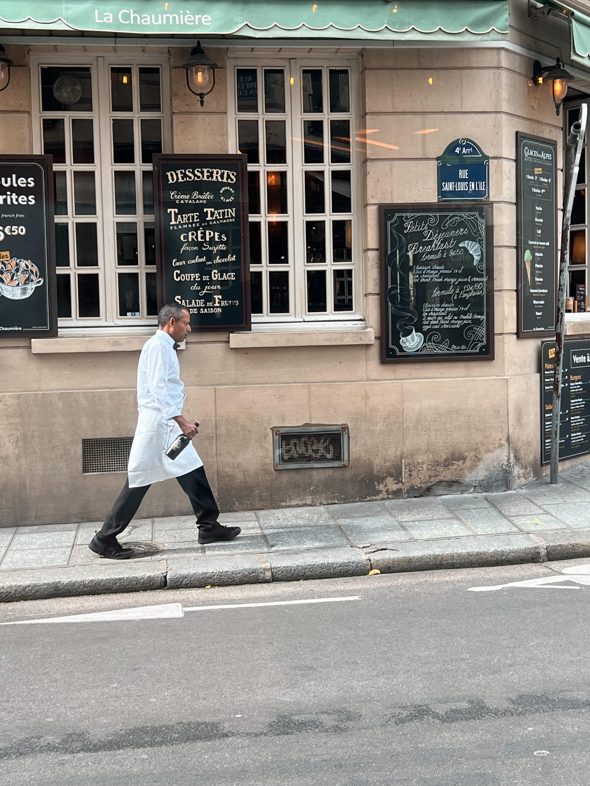 Man walking with bottle in front of a restaurant on ile saint-louis.