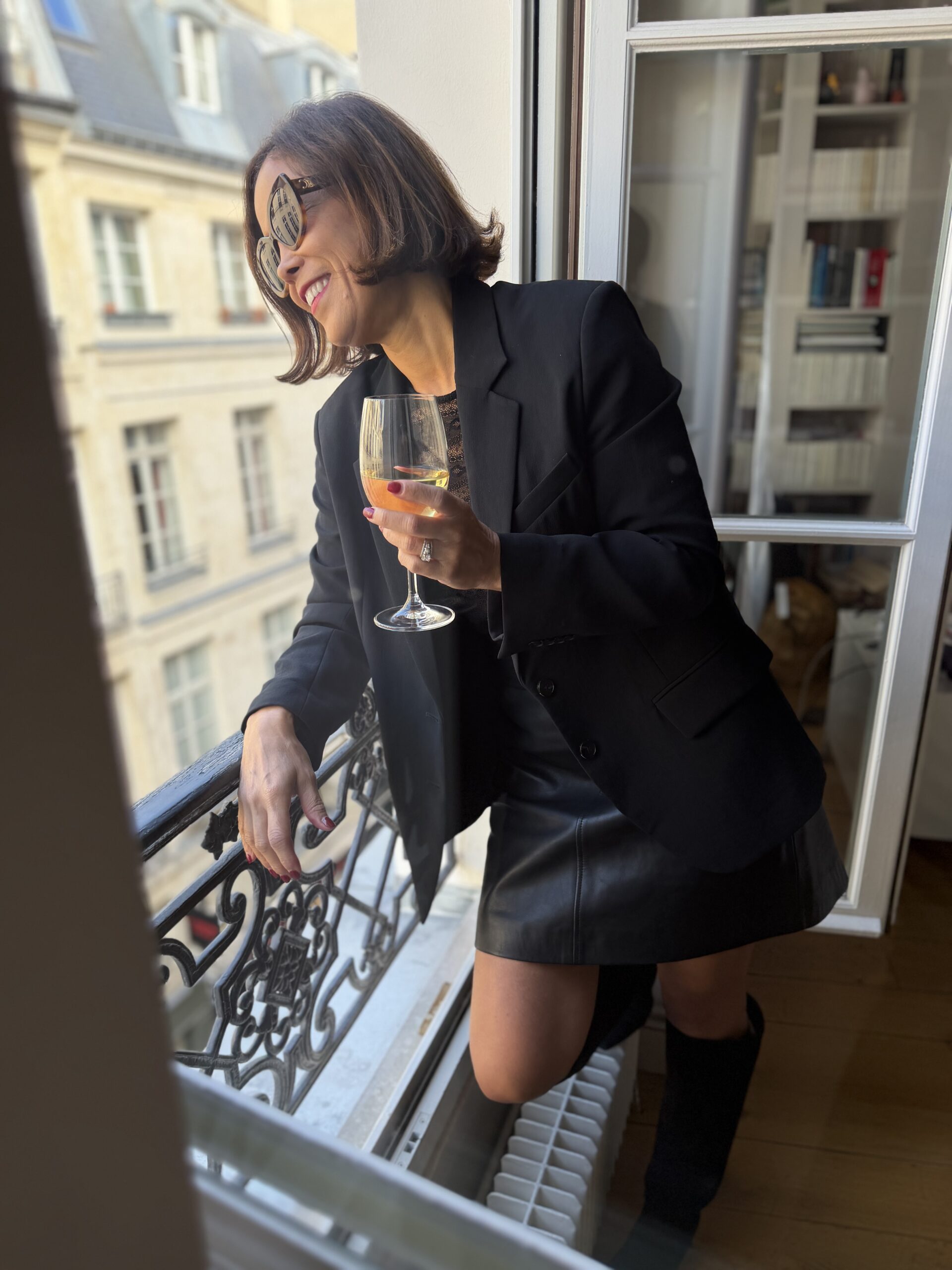 Woman wearing black blazer with leather black skirt and holding a wine glass.