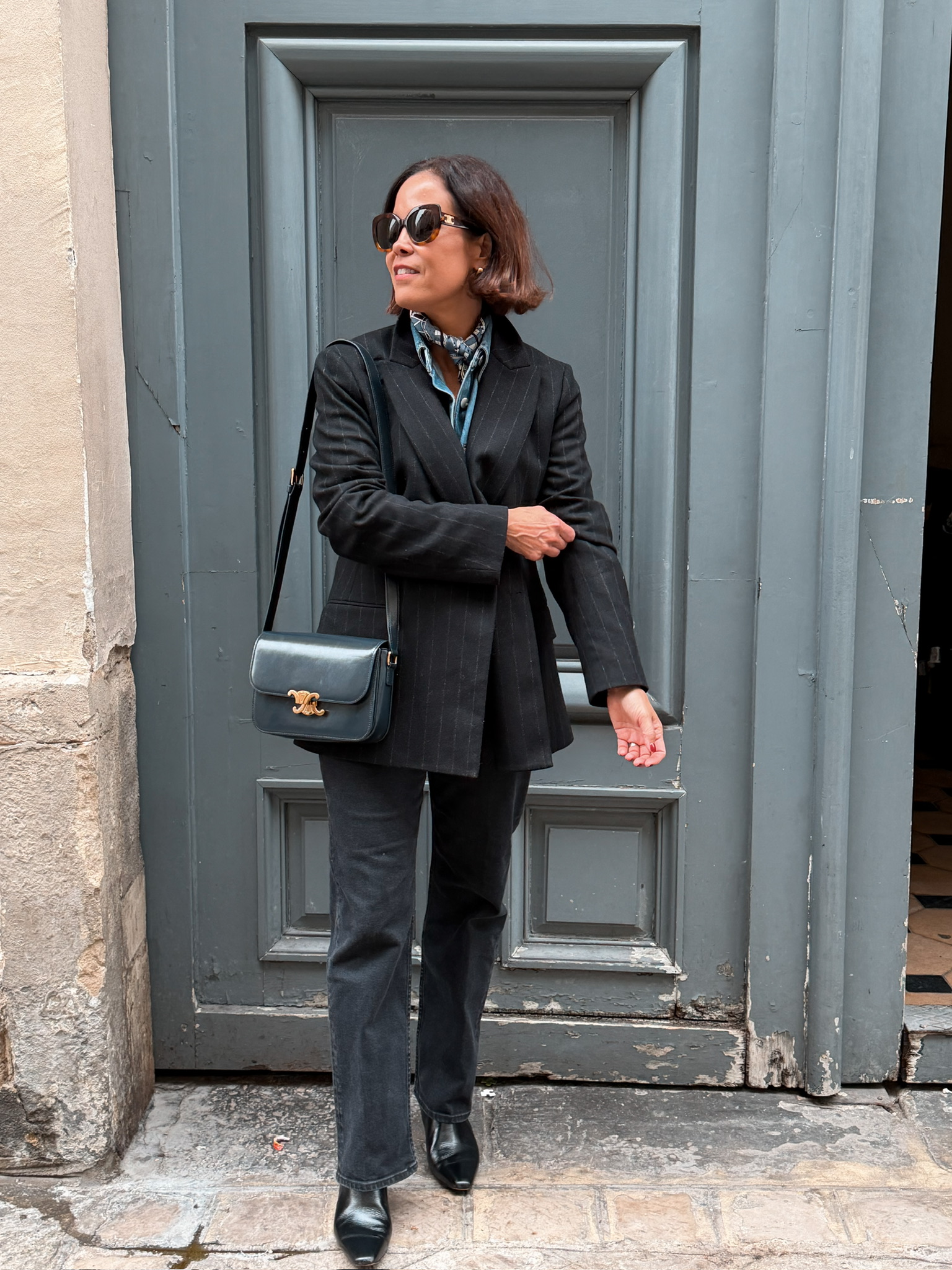 Woman wearing pinstripe blazer with black denim and boots standing in front of a door in fall.
