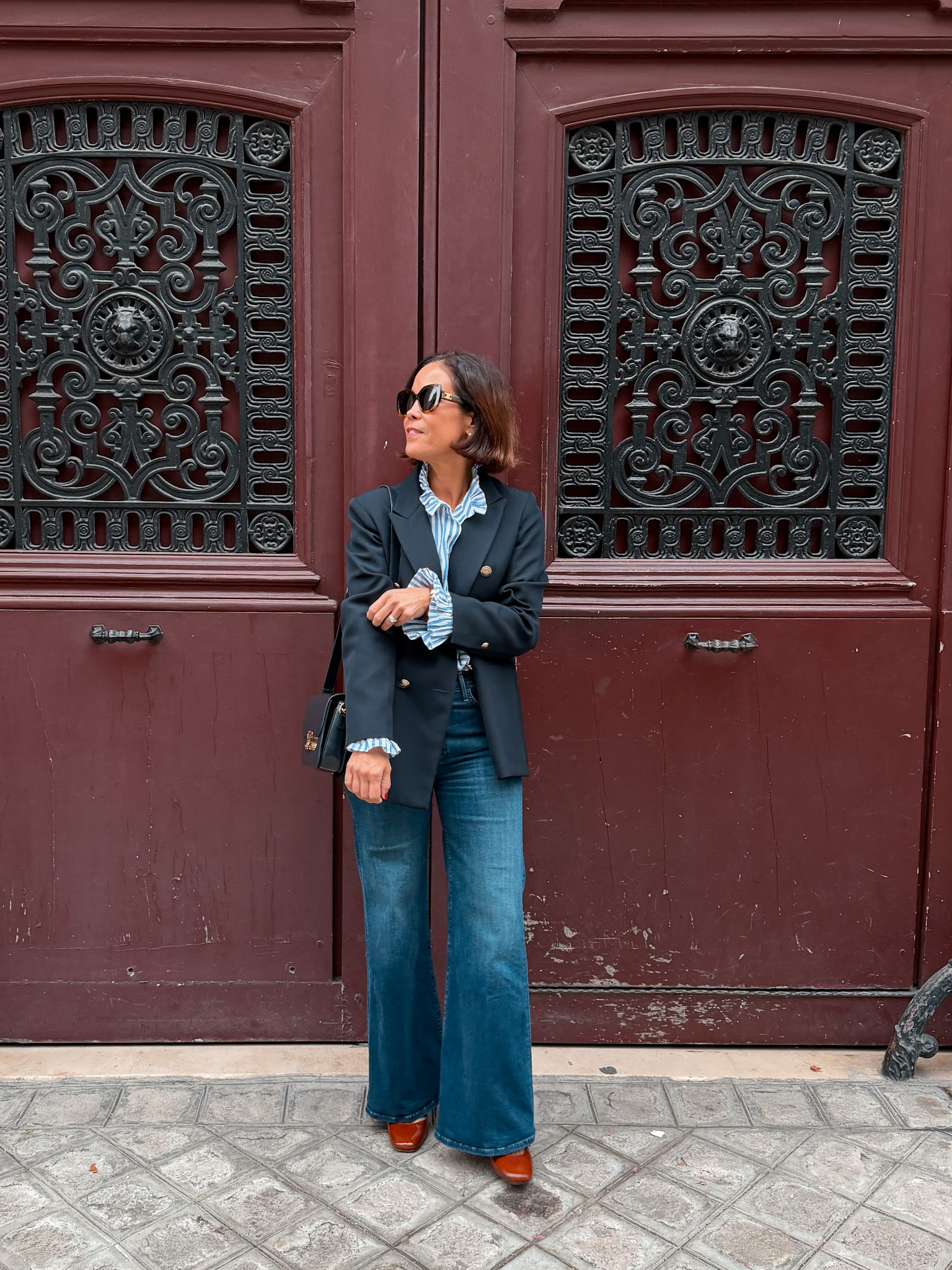 woman in ruffle collar top and navy blouse with denim standing in front of red door in Paris.