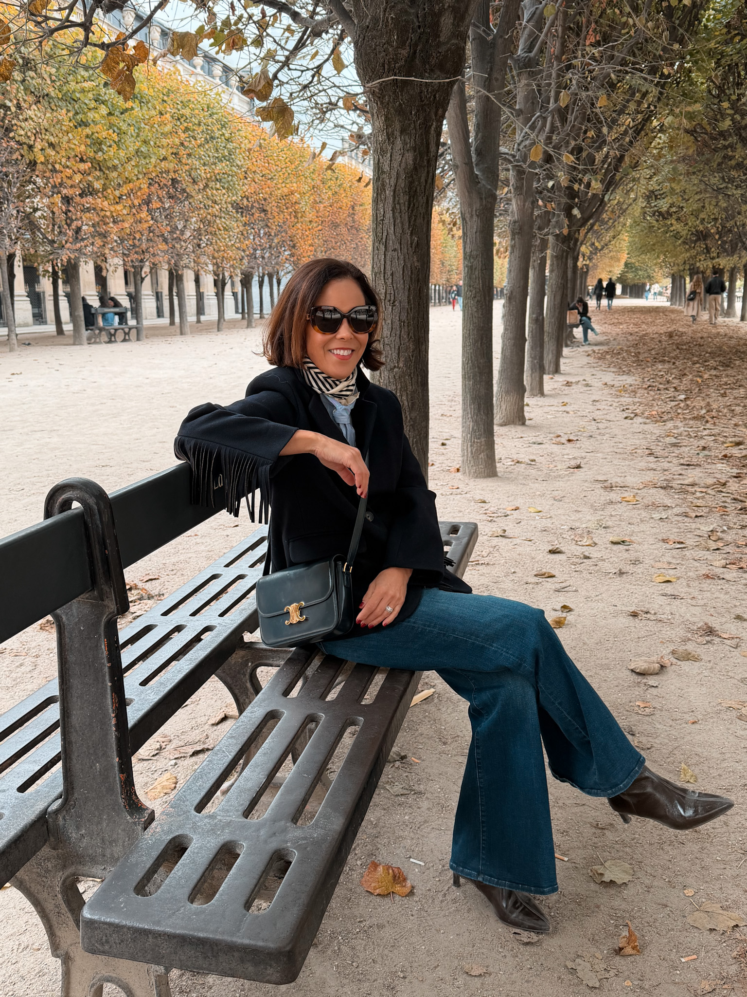 WOMAN WEARING FRINGE JACKET SITTING ON A BENCH IN PARIS.