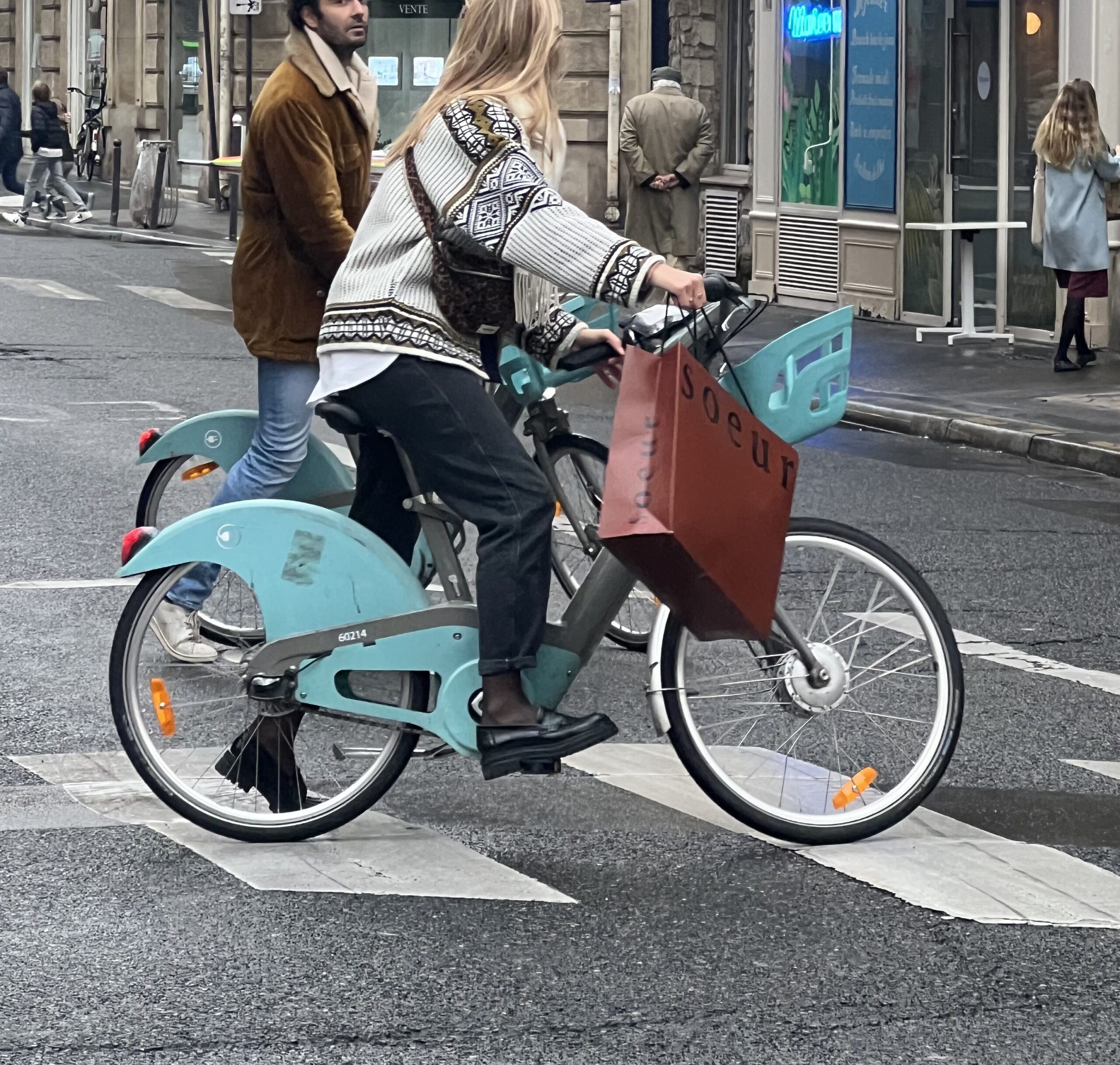 Woman on a bike wearing pants with loafers carrying a bag during fall and autumn.