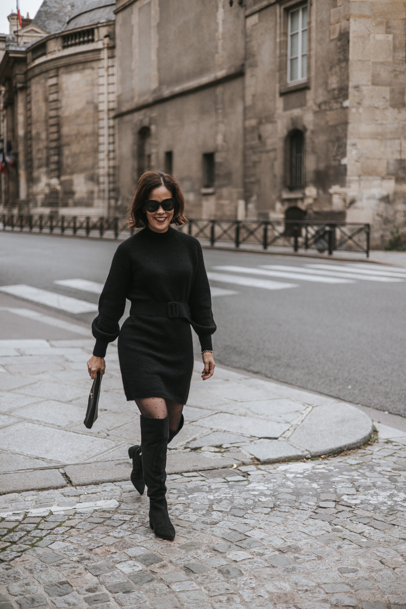 Woman wearing black dress with tall black boots walking down the street in Paris.