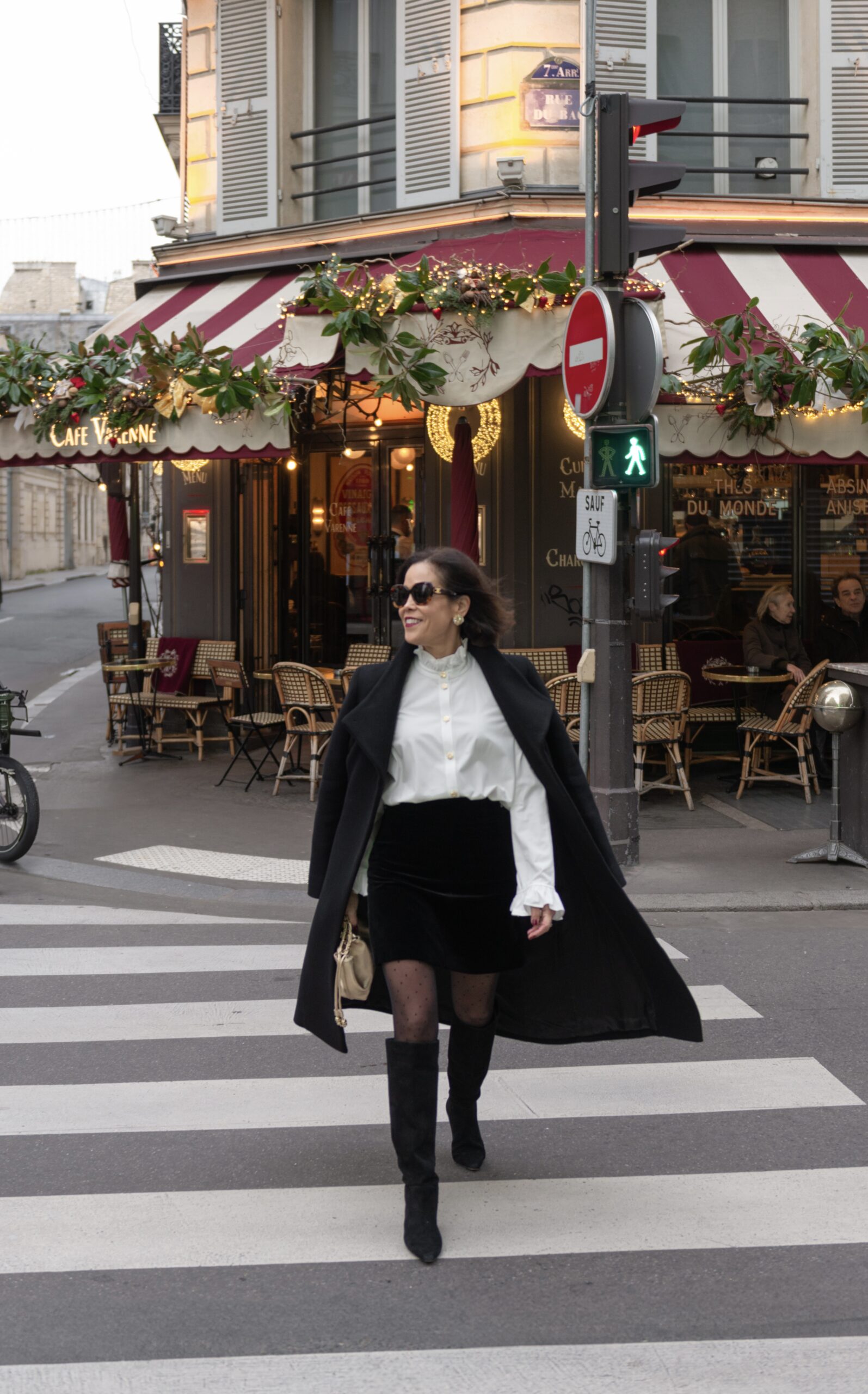 Woman wearing black coat with tall boots and white blouse in Paris showing chic party looks.