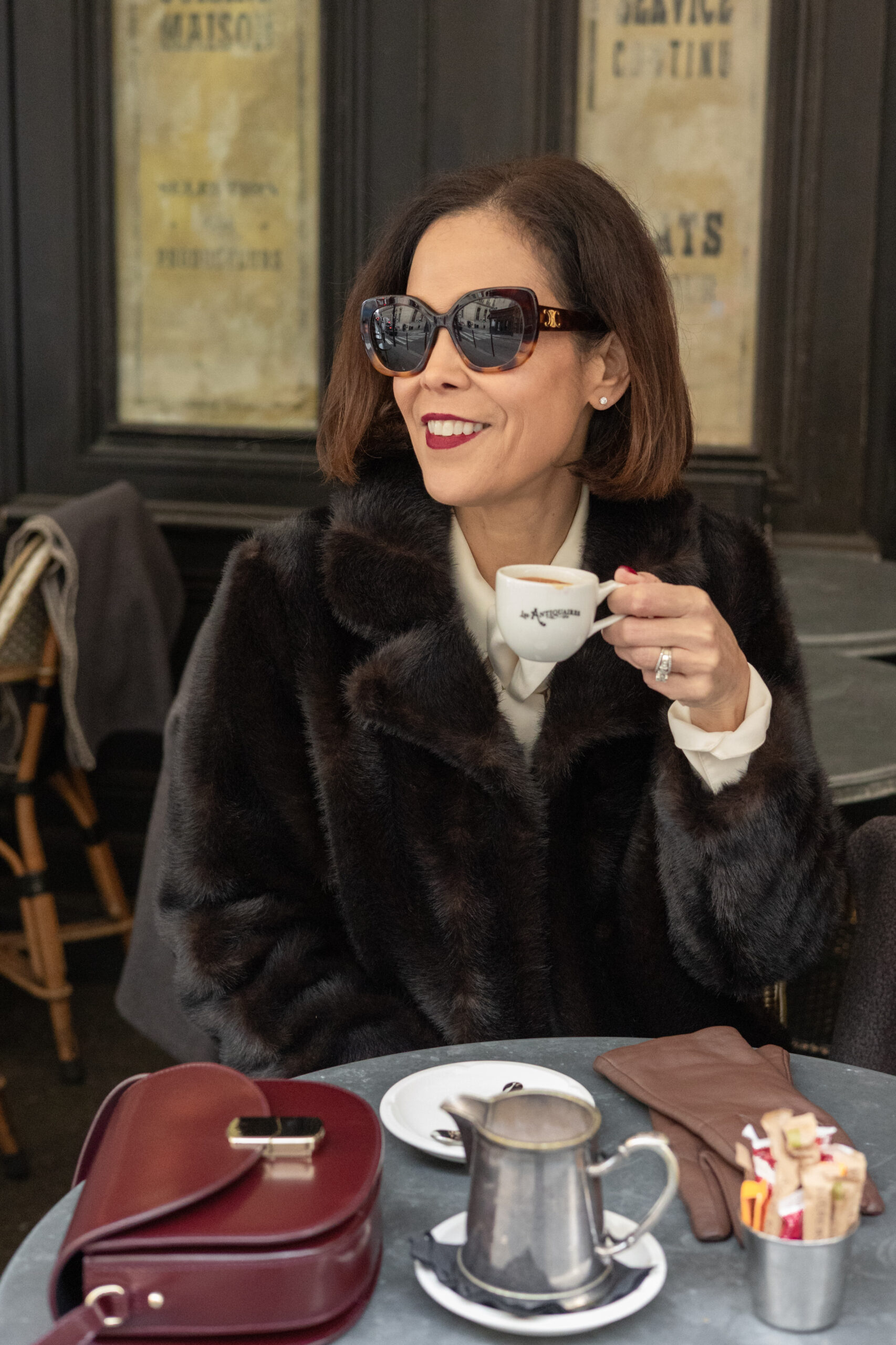 Woman with coffee cup and fur coat sitting at a cafe in Paris.
