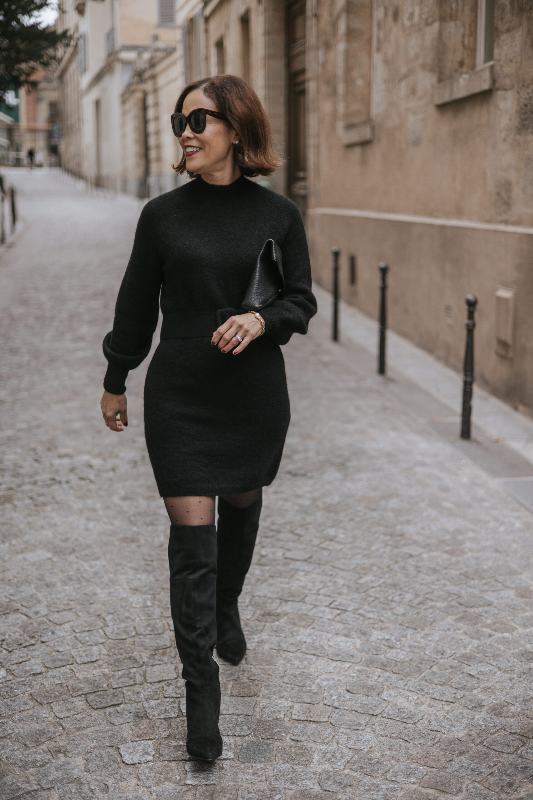 Woman walking in black dress with tall boots.