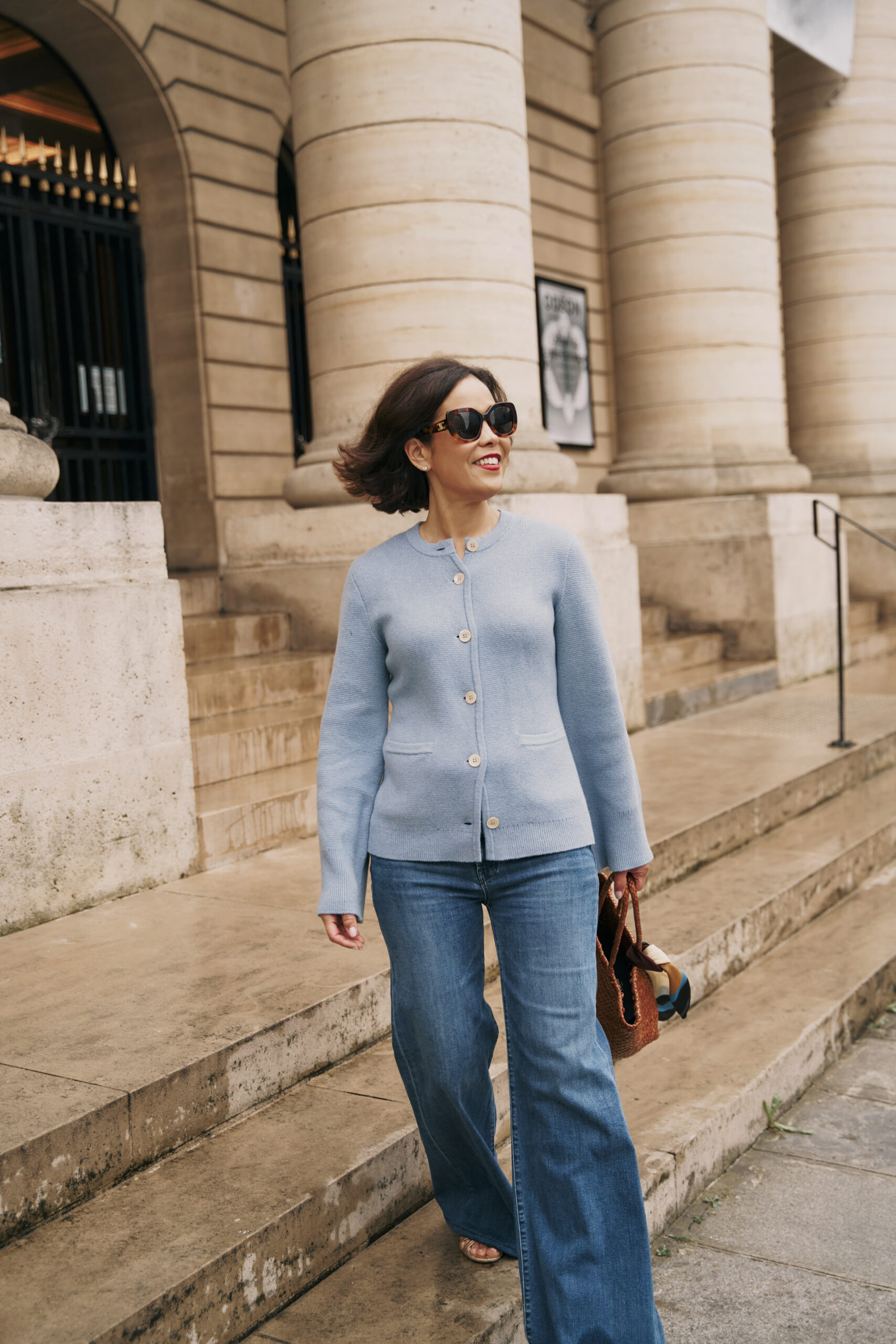 Woman wearing a light blue cardigan and wide-leg jeans while walking confidently in Paris