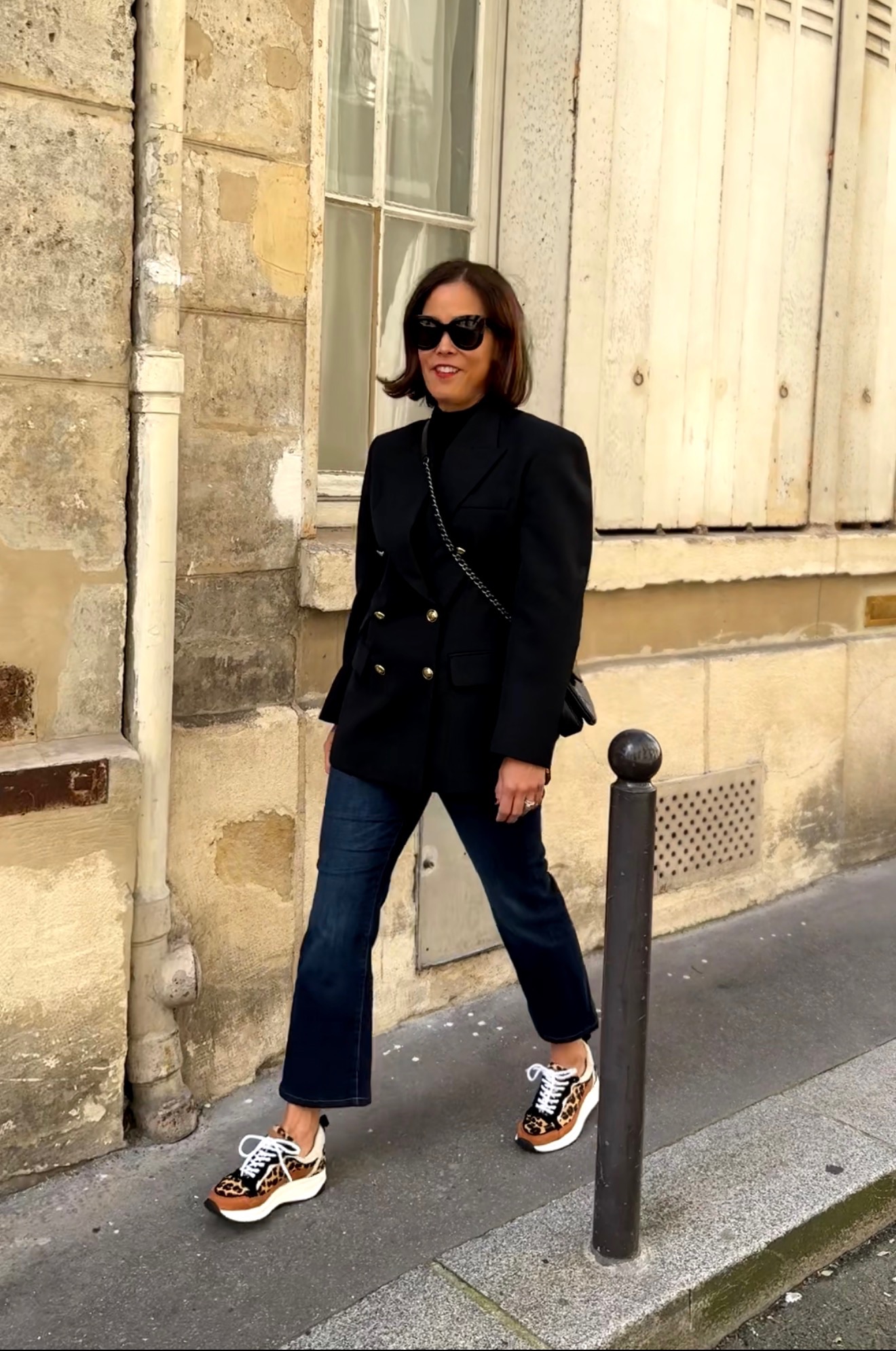 Parisian woman wearing neutral outfit with blazer, jeans, and stylish sneakers while walking in Paris