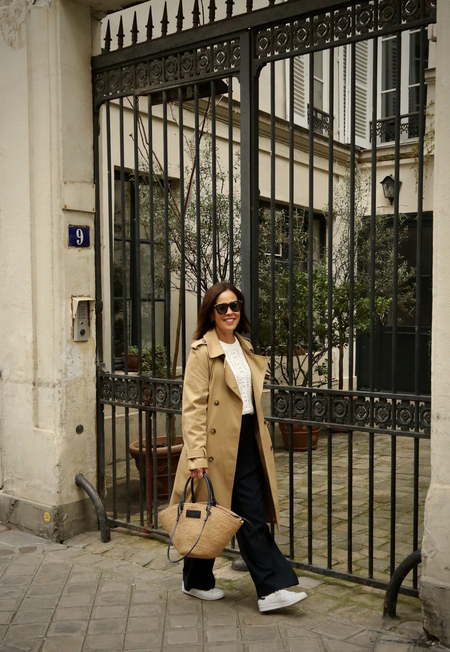 What to wear in Paris in March: trench coat with black pants, a knit sweater, and white sneakers for a chic Paris outfit